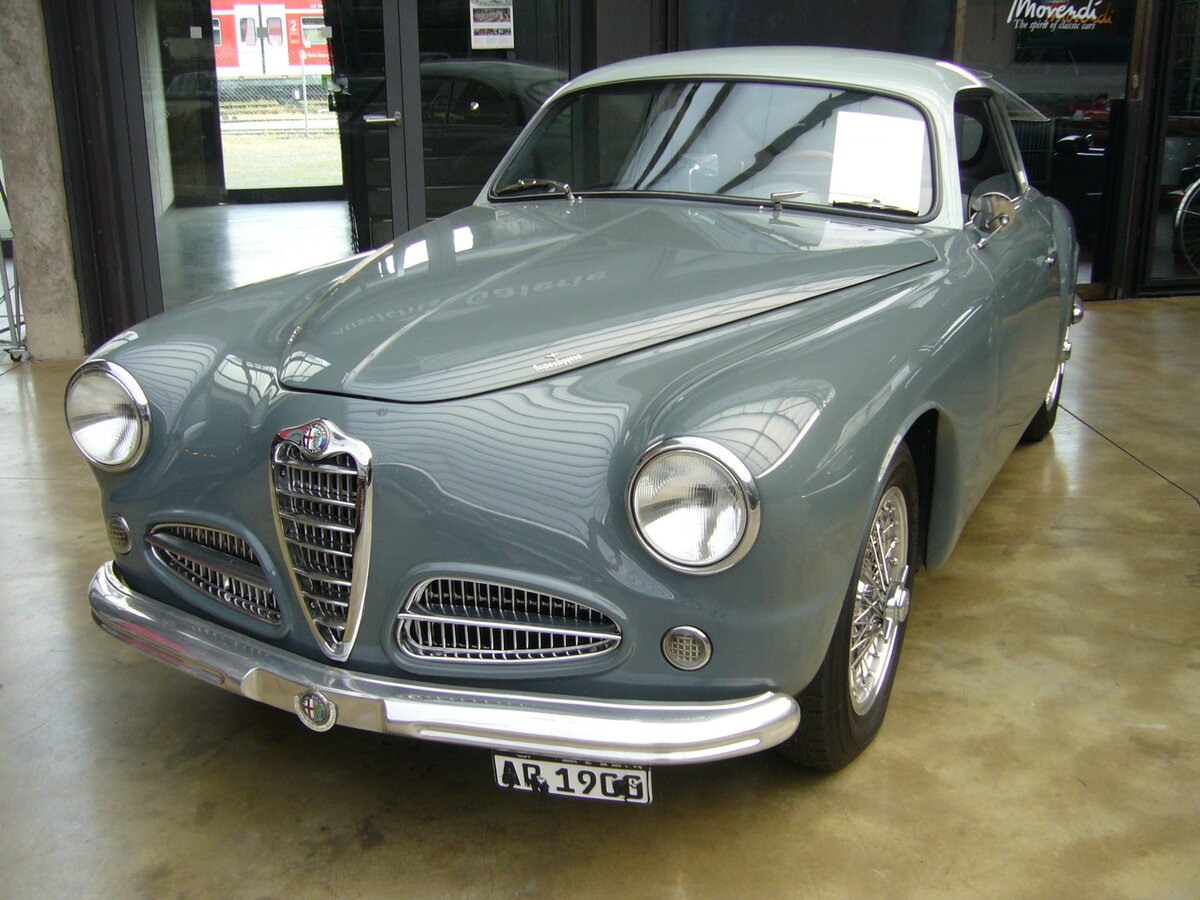 Alfa Romeo 1900C Sprint der Seria uno aus dem ersten Modelljahr 1952. Nach Kriegsende hatte Alfa Romeo lediglich das veraltete Vorkriegsmodell 6C2500 im Programm. Auf staatlichen Druck wurde bei den Milanesen die Entwicklung eines modernen Mittelklassewagens voran getrieben. Das Ergebnis war das Modell 1900. Insgesamt verkaufte man bis 1955 17.243 Limousinen und 1.796 Coupes. Das gezeigte Coupe in der Farbkombination grigio-bicolore wird von einem Vierzylinderreihenmotor mit zwei obenliegenden Nockenwellen angetrieben. Dieser Motor hat einen Hubraum von 1975 cm³ und leistet 115 PS. In zahlreichen Straßenrennen erwies sich das 190 km/h schnelle Coupe als unschlagbar. Classic Remise Düsseldorf am 07.06.2021.