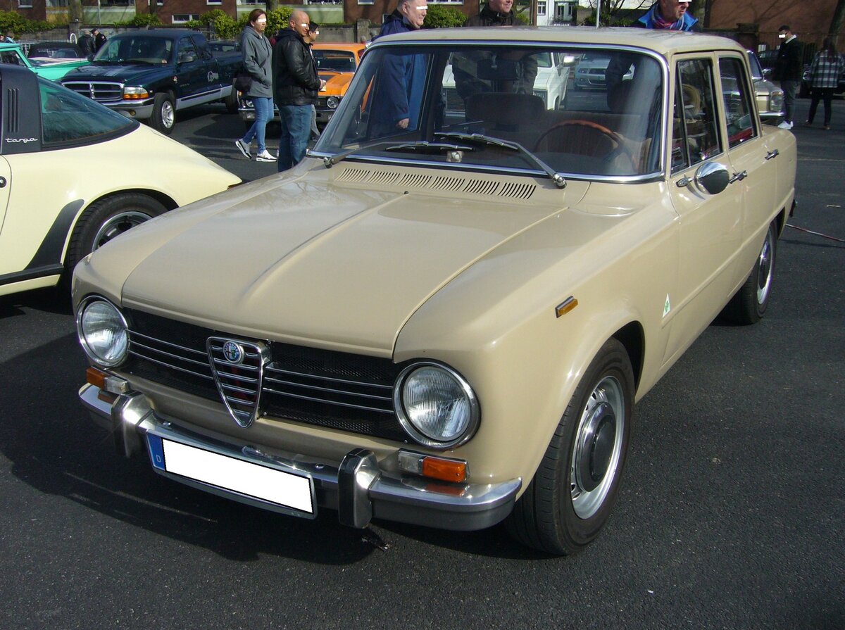 Alfa Romeo Giulia 1300 Super im Farbton beige carva, gebaut in den Jahren von 1964 bis 1971. Um, die im Jahr 1962 vorgestellte Giulia, auch weniger betuchten Kunden zugänglich zu machen (billig war die Giulia ja nie), bot man ab 1964 diese spartanischer ausgestattete Version mit einem 1.3l Motor an. Der Vierzylinderreihenmotor mit Doppelnockenwellen hat einen Hubraum von 1290 cm³ und leistet zwischen 85 PS und 89 PS. Das gezeigte  Julchen  stammt aus dem Jahr 1971. Oldtimertreffen an Mo´s Bikertreff in Krefeld am 10.03.2024.