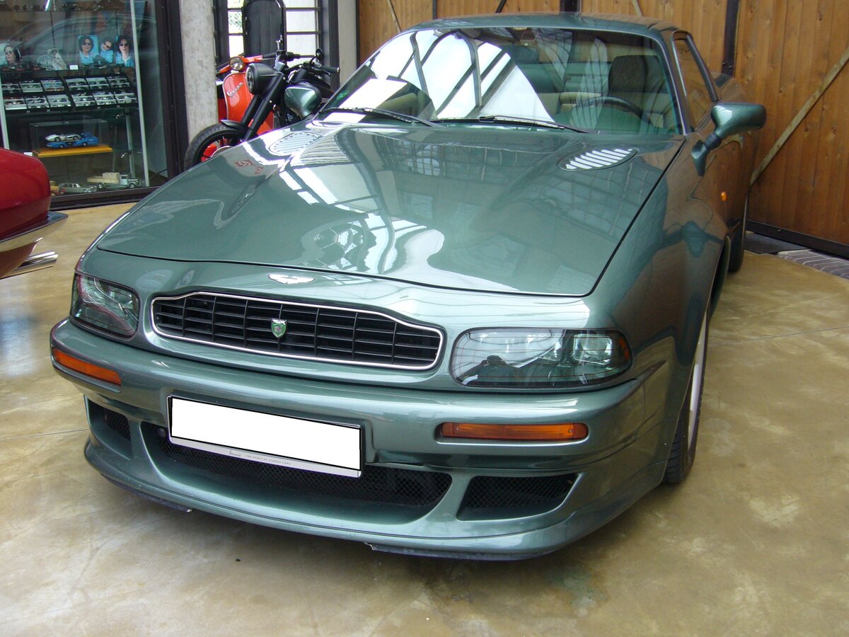 Aston Martin V8 Vantage V600. Das Luxuscoupe Vantage wurde im Jahr 1996 als Nachfolger des Aston Martin Virage vorgestellt. Das Modell war als Coupe und Cabriolet namens V8 Volante Vantage lieferbar. Ab dem Jahr 1998 konnte der Kunde dann das aufgerüstete Modell V8 Vantage V600 bestellen. Dieses Modell wurde beim Aston Martin Service Department technisch noch mehr optimiert. Unter anderem erhielt der Kompressor größere Schaufelblätter, einen geänderten Ladedruck und einen speziellen Auspuff aus Edelstahl. In der Regel waren die V600 Modelle im Farbton AM racing green lackiert. Der V8-Motor hat einen Hubraum von 5341 cm³ und leistet 608 PS. Classic Remise Düsseldorf am 12.07.2022.