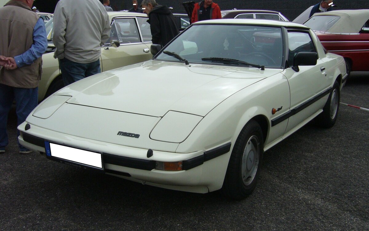 Mazda RX7 der Baureihe FB2. Der Mazda RX7 kam 1979 auf den Markt und schien dem Porsche 924 wie aus dem Gesicht geschnitten zu sein. Auf dem Hauptabsatzmarkt dieses Modelles, den USA, kamen auf einen verkauften Porsche 924 zehn verkaufte RX7, da dieser rund US$ 7000,00 günstiger war als der Konkurrent aus Zuffenhausen. Das gezeigte Auto dürfte von 1981 bis 1983 gebaut worden sein, da es mit den auffälligen Rotary-Felgen (die den Kreiskolbenmotor symbolisieren) ausgerüstet ist. Der Zweischeibenwankelmotor hat ein Kammervolumen von zweimal 573 cm³ und leistete anfänglich 105 PS. Ab November 1980 erhöhte sich die Leistung auf 115 PS. Das Modell wurde im Februar 1986 durch ein Nachfolgemodell abgelöst. Oldtimer- und Youngtimertreffen an Mo´s Bikertreff in Krefeld am 08.10.2023.