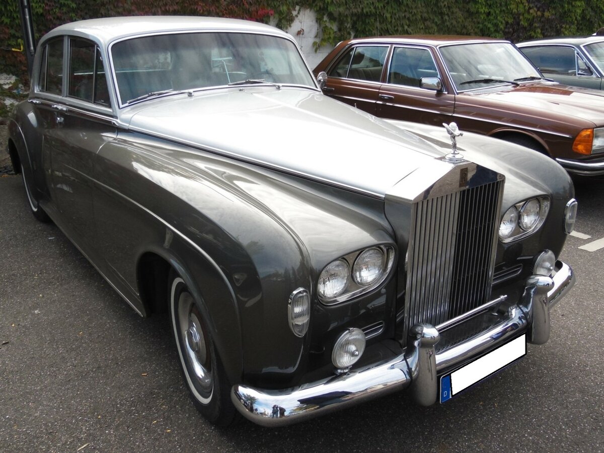 Rolls Royce Silver Cloud III in der Farbkombination shell grey over royal garnet, gebaut in den Jahren von 1962 bis 1965. Um Sonderaufbauten wie Cabriolets, Shooting Brakes und Convertibles herzustellen , wurde das Chassis sogar bis 1966 ausgeliefert. Designänderungen gegenüber des Vorgängermodelles  Silver Cloud II  wie der Wechsel zu Doppelscheinwerfern und eine niedrigere Linienführung der vorderen Kotflügel und der Motorhaube waren die größten Unterschiede, als gegen Ende 1962 der  Silver Cloud III  vorgestellt wurde. Die Nachfrage war so groß, dass sogar Extraserien bis in das Jahr 1966 hinein gefertigt wurden, obwohl das Nachfolgemodell  Silver Shadow  bereits 1965 sein Debüt gegeben hatte. Insgesamt verließen 2.809 Autos dieses Typs die Werkshallen in Crewe, davon 254 Autos mit langem Radstand. Der V8-Motor hat einen Hubraum von 6230 cm³ und leistet 187 PS. Herbstfest an der Düsseldorfer Classic Remise vor einigen Jahren.