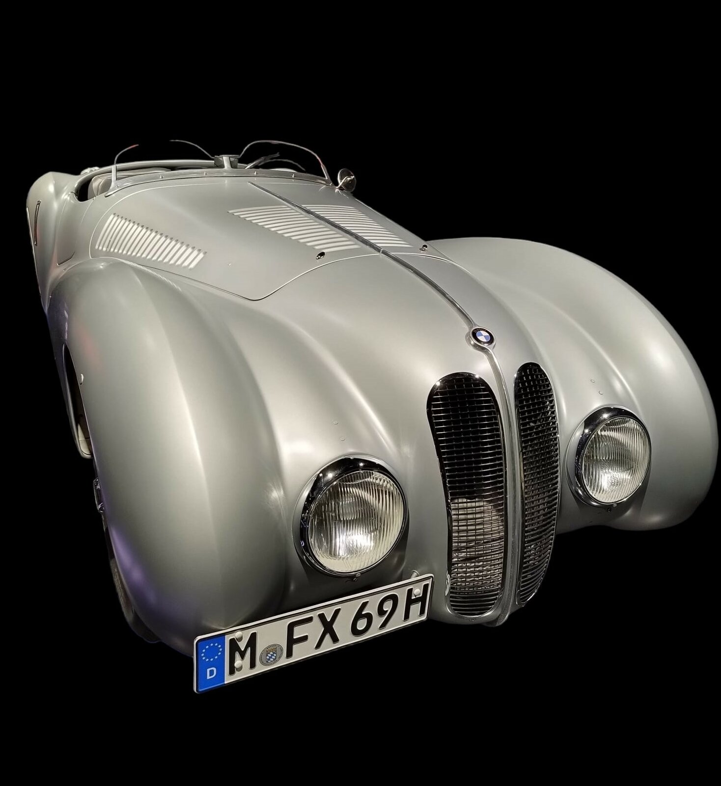 Der Erfolg der Marke BMW im Rennsport begann früh. Kurz nach Beginn der Produktion des BMW 328 im Jahr 1936 nahm BMW mit dem Wagen an Rennen teil. Der Sechszylinderreihenmotor mit einem Hubraum von 1971 cm³ leistete bis zu 136 PS und verhalf dem Auto mit der leichten, aerodynamischen, Aluminiumkarosserie zu etlichen Rennsiegen. Das Auto wog nur erstaunliche 700 Kilogramm. Viele andere Autohersteller übernahmen die eleganten, geschwungenen, Kotflügel und das sich verjüngende Heck. Bei der Mille Miglia des Jahres 1940 wurde dieses Auto Dritter. Gefahren wurde der Wagen von Adolf Brudes (*1899 +1986) und Ralph Roese (*1900 +1950). Sieger wurde ebenfalls ein BMW 328, allerdings mit einer Coupe-Karosserie der Carrozzeria Touring/Mailand. Am Steuer des Siegerwagens saß Huschke von Hanstein (*1911 +1996) und Walter Bäumer (*1908 +1941). BMW-Museum München im Juli 2022.