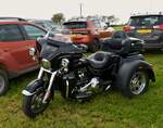 Trike Harley-Davidson Tri Gilde, gesehen auf einem Wiesenparkplatz bei einer Veranstaltung.