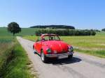 Roter VW-Käfer-1302 Cabrio braust durch die grüne Landschaft;  150604