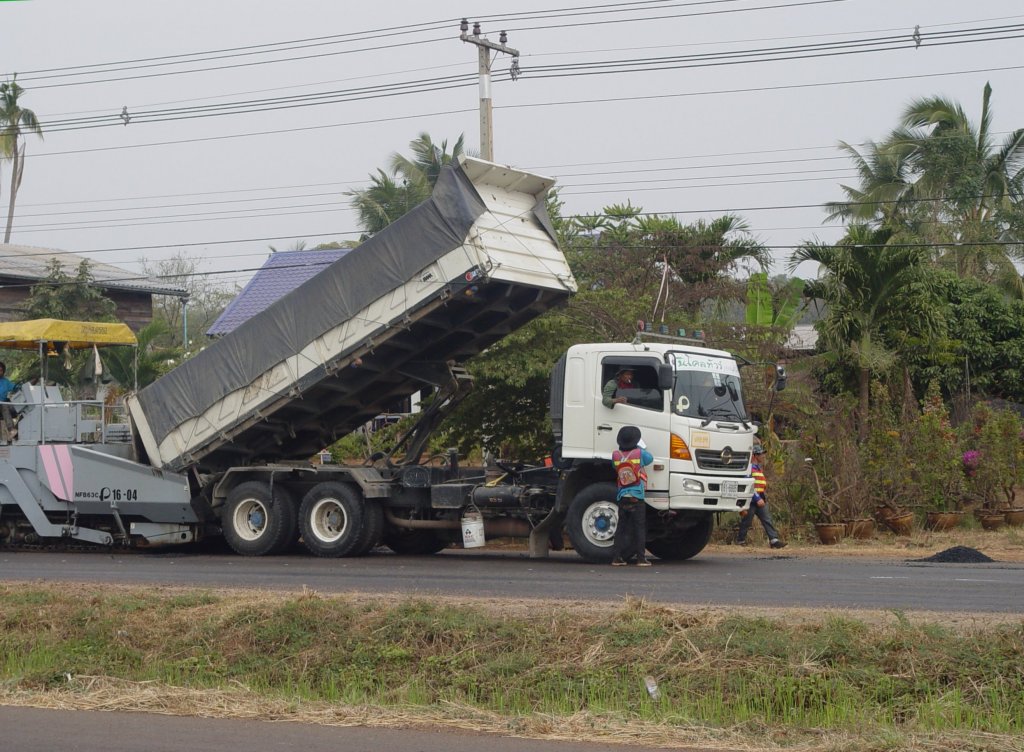 Ein HINO 3-Achs-Kipper hat Asphalt angeliefert und befllt damit eine Asphaltiermaschine bei der Stadt Nang Rong im Nordosten Thailands am 17.01.2011