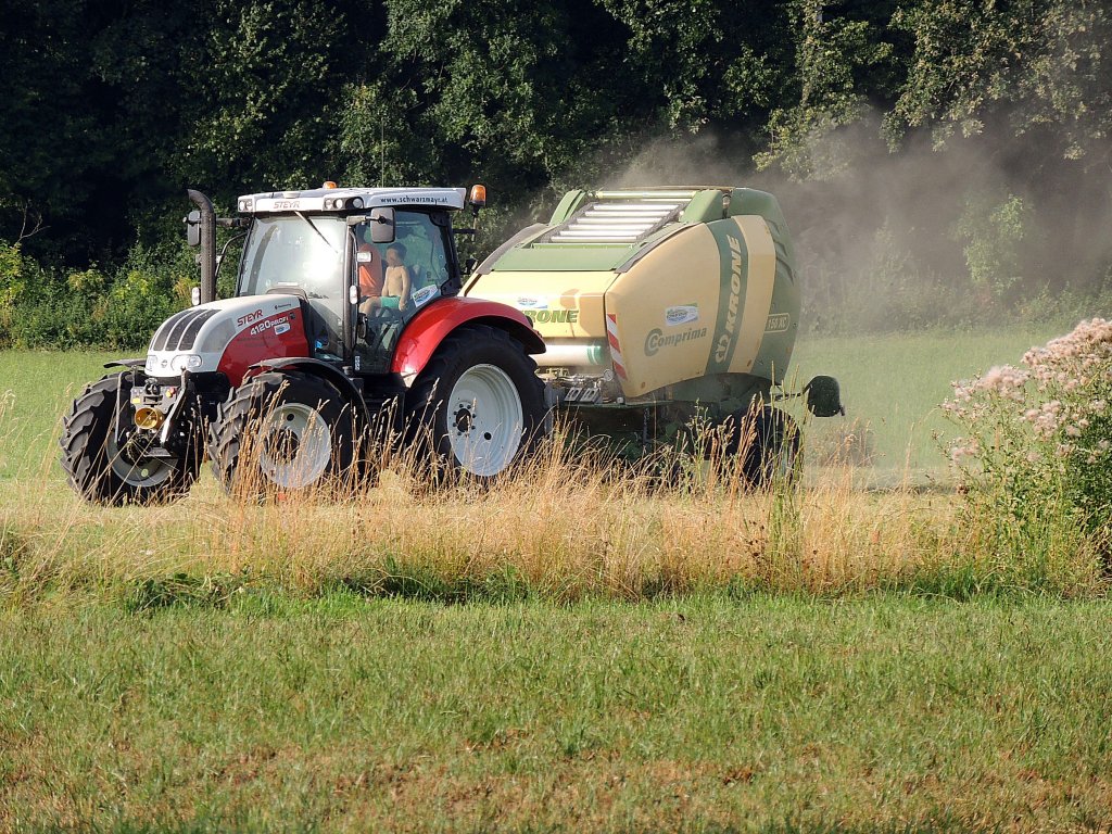 STEYR 4120-Profi holt mit der KRONE-Comprima V150XCI Rundballenpresse noch die letzten Heureste von der Wiese; 130803