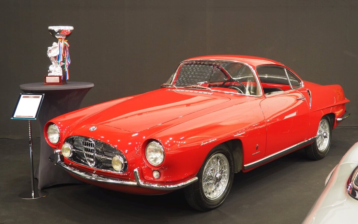 Alfa Romeo 1900 CSS Ghia Speciale aus dem Jahr 1954.
Der Alfa Romeo 1900 war das erste, von Alfa Romeo neu entwickelte Fahrzeug nach WW2 und zugleich das erste Modell mit einer selbsttragenden Karosserie. Der Wagen wurde im Oktober 1950 auf dem Pariser Salon vorgestellt. Zunächst mit einem 80 PS starken Vierzylinderreihenmotor. Im Jahre 1954 wurde der Motor mit obenliegenden Nockenwellen weiterentwickelt und leistete fortan in der Version Super Sprint (SS) befeuert durch zwei Solex-Fallstrom-Dopplervergaser etwa 115 PS. Für die damals noch zahlreich vertretenen unterschiedlichen und unabhängigen Karosseriebauunternehmen, wie Touring, Bertone, Zagato, Pininfarina und Ghia, baute Alfa Romeo eine reine Chassisversion mit verkürztem Radstand. Den C für corto = kurz. So entstanden etliche Aufbauten des 1900 C, wie dieser von der Carrozzeria Ghia. Der hier gezeigte 1900 CSS Ghia Special ist die Nummer 4 von 12 Exemplaren, die bei Ghia gebaut wurden. Es sind nur zehn dieser Fahrzeuge weltweit bekannt. Die verschiedenen Autos gleichen sich nur oberflächlich und sind in vielen Details unterschiedlich. Dieser Wagen wurde in Mailand erstmalig zugelassen. Von 1960 bis 1998 hatte der Alfa den selben Besitzer. 2007 wurde der Alfa nach Deutschland verkauft und ab 2008 vollständig restauriert. Der Vierzylinderreihenmotor hat einen Hubraum von 1993 cm³ und leistet 115 PS. Die Höchstgeschwindigkeit soll bei 180 km/h liegen.
Dieses Auto war übrigens  The best of Show  der Techno Classica Essen 2022. Techno Classica Essen am 27.03.2022.