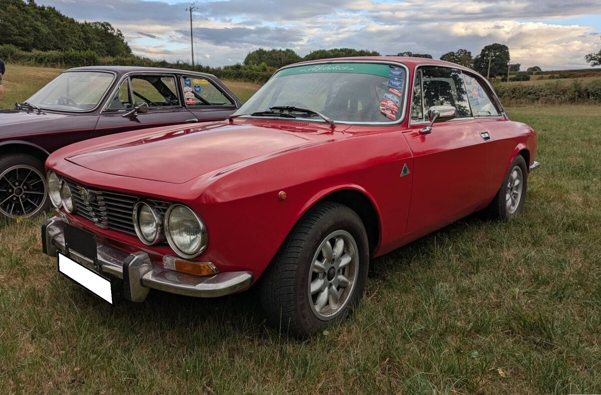 Alfa Romeo 2000 GT Veloce (kurz GTV), produziert in den Jahren von 1971 bis 1976. Der in 44.301 Einheiten produzierte 2000 GTV war das Spitzenmodell der bereits seit 1963 gebauten  Junior  Modell-Reihe. Motorisiert mit einem Vierzylinderreihenmotor mit einem Hubraum von 1.962 cm� und einer Leistung von 131 PS machten diesen, damals noch erschwinglichen Sportwagen, 200 km/h schnell. Der gezeigte, rechts gelenkte, 2000 GTV wurde 1972 erstmalig zum britischen Stra�enverkehr zugelassen und d�rfte im beliebten Farbton 501/rosso alfa lackiert sein. Treffen des Chainbridge classic car club auf der Wiese vor einem Pub in Chainbridge/Wales im Juli 2025.