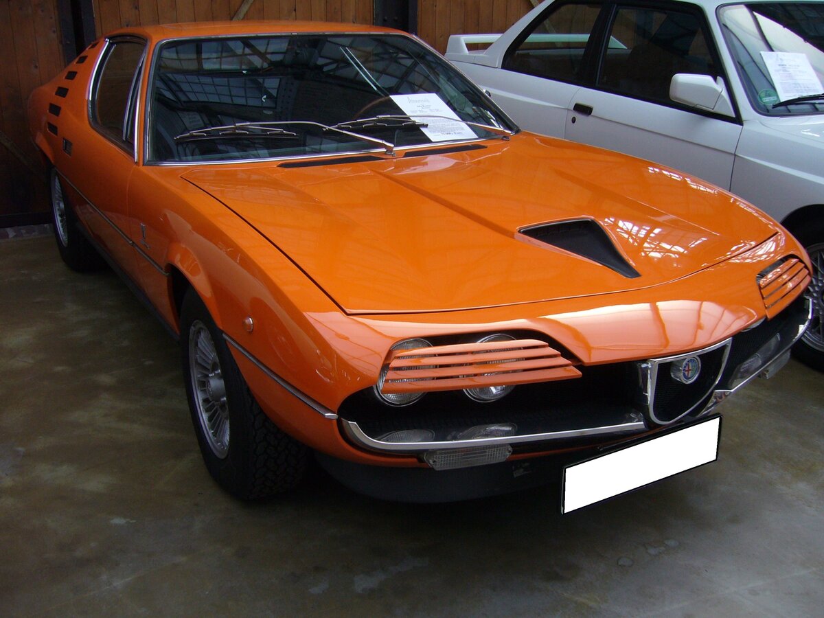 Alfa Romeo Montreal im Farbton arancio 601. Produziert wurden von 1970 bis 1977 insgesamt 3917 Autos dieses Typs. Der Wagen wurde als Designstudie im Jahr 1967 auf der Weltausstellung (Expo) in Montreal vorgestellt. Da dieser hübsche Sportwagen großen Anklang fand, ging er ab 1970 in Serie. Den Namen seines Vorstellungsortes behielt er bei. Der V8-Motor hat einen Hubraum von 2.593 cm³ und leistet 200 PS. Das Fahrwerk wurde vom Typ 105 (Giulia) übernommen. Classic Remise Düsseldorf am 12.09.2022.