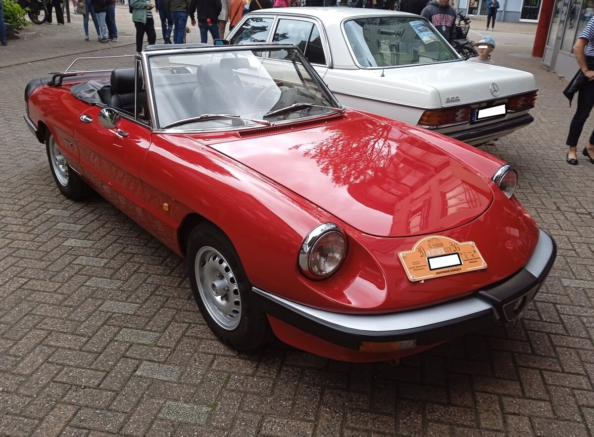 Alfa Romeo Spider 2.0 im Farbton rosso alfa aus dem Jahr 1987. Gereift und erwachsen bestritt der Spider sein zweites Lebensjahrzehnt. Optisch gab es nun deutliche Ver�nderungen. Kunststoffsto�f�nger mit einem integrierten Grill vorne, ein un�bersehbarer Kunststoffheckspoiler und einen  modernisierter  Innenraum sollten das  Aerodinamica  getaufte Auto aktuell erscheinen lassen. Sp�tter nannten es allerdings lieblos  Gummilippe . Die Baureihe war von 1986 bis 1989 im Verkaufsprogramm von Alfa Romeo. Der Vierzylinderreihenmotor hat einen Hubraum von 1962 cm� und leistet 125 PS, bzw. 115 PS wenn ein Katalysator verbaut war. 13. Saarner Oldtimer-Cup am 30.08.2026 in M�lheim an der Ruhr/Saarn.