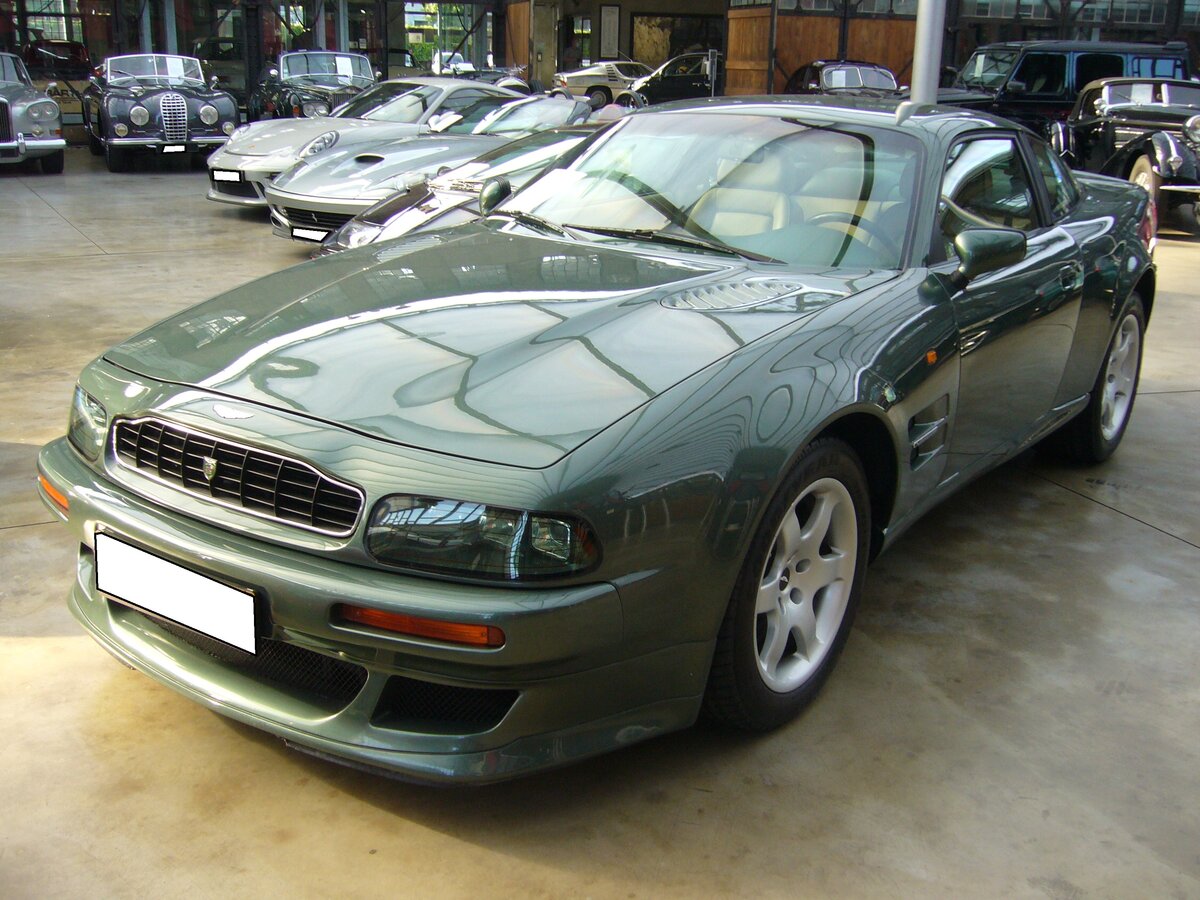 Aston Martin V8 Vantage V600. Das Luxuscoupe Vantage wurde im Jahr 1996 als Nachfolger des Aston Martin Virage vorgestellt. Das Modell war als Coupe und Cabriolet namens V8 Volante Vantage lieferbar. Ab dem Jahr 1998 konnte der Kunde dann das aufgerüstete Modell V8 Vantage V600 bestellen. Dieses Modell wurde beim Aston Martin Service Department technisch noch mehr optimiert. Unter anderem erhielt der Kompressor größere Schaufelblätter, einen geänderten Ladedruck und einen speziellen Auspuff aus Edelstahl. In der Regel waren die V600 Modelle im Farbton AM racing green lackiert. Der V8-Motor hat einen Hubraum von 5341 cm³ und leistet 608 PS. Classic Remise Düsseldorf am 28.09.2021.