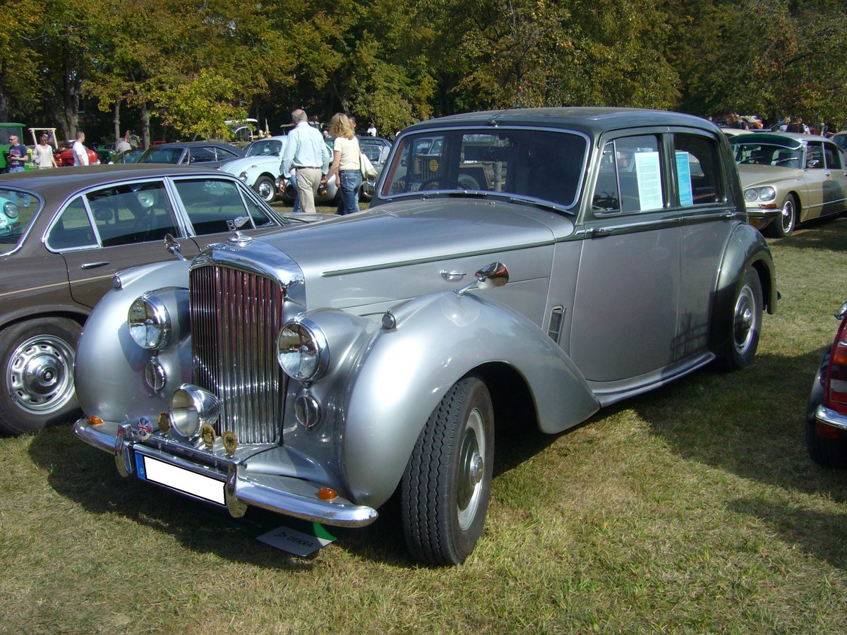 Bentley MK6 Saloon mit Werkskarosserie aus dem Jahr 1952. Von diesem Modell wurden von 1946 bis 1952 5201 Fahrzeuge produziert. Der Kaufpreis betrug im Jahr 1952 4391,00 englische Pfund. Diese Summe entsprach nach dem damaligen Wechselkurs DM 51.000,00. Ein horrender Preis, wenn man bedenkt das ein VW Käfer in der Exportausstattung zum gleichen Zeitpunkt mit einem Kaufpreis von DM 5.150,00 zu Buche schlug. Dafür hatte der Wagen aber auch solch nette Extras wie ein serienmäßigen Picknicktisch, eine Minibar im Fond, sowie ein Schiebedach. Angetrieben wird das zwei Tonnen schwere Fahrzeug von einem Sechszylinderreihenmotor, der aus einem Hubraum von 4566 cm³ ca. 150 PS leistet. Oldtimertreffen des Oldtimerclubs Schermbeck am 22.09.2019 in Lühlerheim. 
