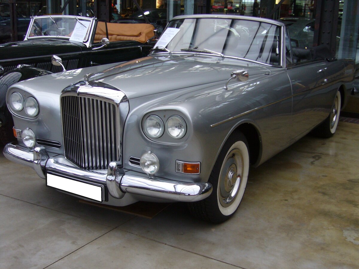 Bentley S3 Continental DHC (D rop H ead C oupe) aus dem Jahr 1964. Der gezeigt Wagen verließ als Chassis im Spätherbst 1964 das Werk und wurde an Mulliner Coachworks/London überführt. Hier bekam der Wagen seine Cabioletkarosserie mit den markanten vorderen Scheinwerfern, den so genannten  Chinese eyes . Angetrieben, wird, der im Farbton sheel grey lackierte Wagen, von einem V8-Motor, der aus einem Hubraum von 6141 cm³ 178 PS leistet. Classic Remise Düsseldorf am 23.11.2021.