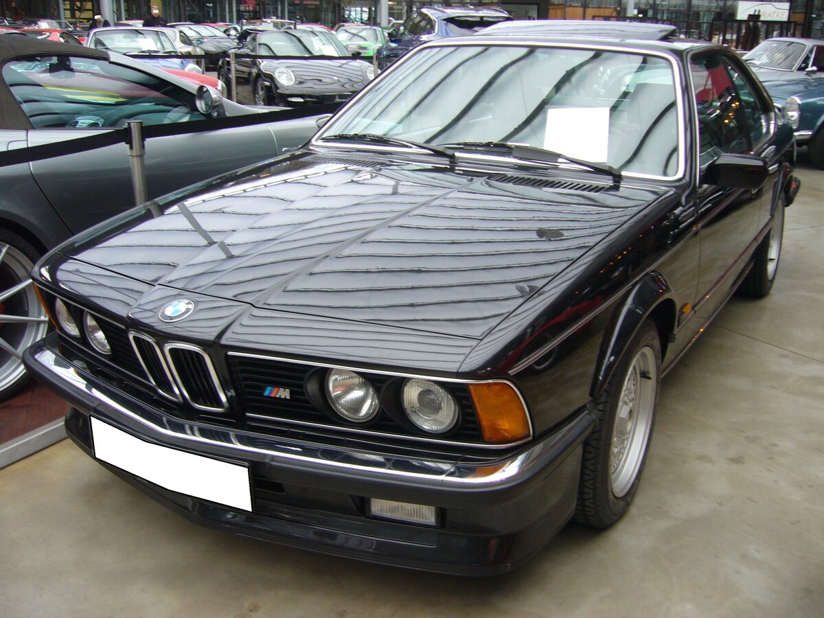 BMW E24 635CSi M6 aus dem Jahr 1985 im Farbton diamantschwarzmetallic. Das BMW 6´er Coupe der Baureihe E24 wurde im März 1976 auf dem Genfer Auto Salon vorgestellt und bis 1989 produziert. Das Coupe war mit etlichen Motorisierungen lieferbar. Spitzenmodell war jedoch der abgelichtete 635 CSi M6, der ab Frühjahr 1984 bei den Händlern stand. Äußerlich unterscheidet er sich vom  normalen 635CSi  durch eine tiefer herunter gezogene Frontschürze. Unter der Haube ist der Motor des BMW M1 verbaut. Dieser Sechszylinderreihenmotor mit Vierventiltechnik hat einen Hubraum von 3453 cm³ und leistet 286 PS. Die Höchstgeschwindigkeit wurde von BMW mit 255 km/h angegeben. Für ein solches Auto war bei seiner Markteinführung ein Kaufpreis von mindestens DM 102.050,00 fällig. Classic Remise Düsseldorf am 26.02.2024.
