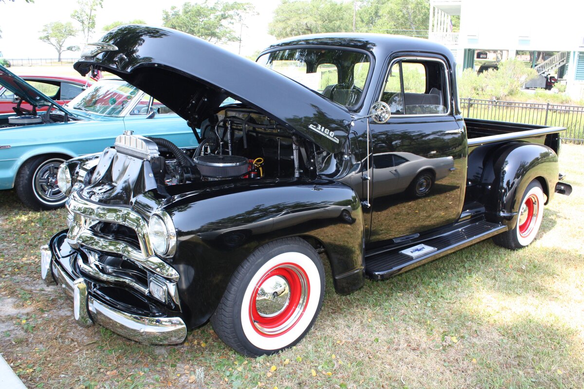 Chevrolet 3100 Pickup Truck aus dem Jahr 1954 im Farbton onyx black. Die Series 3100 Pickup-Modelle wurden im Mai 1947 von Chevrolet als neue Nutzfahrzeug-Linie vorgestellt.
Dieses völlig neu konstruierte Modell ersetzte die Chevrolet AK-Serie, die ab 1941 produziert wurde. Typisch für diese Trucks waren, die in die vorderen breiten Kotflügel integrierten Scheinwerfer und die hohe Motorhaube. Bis ins Modelljahr 1953 hatte das Modell auch noch eine geteilte Windschutzscheibe. Das als Unisteel-Kabine bezeichnete Führerhaus des Chevrolet 3100 im so genannten  Advance Design  besaß eine durchgehende Sitzbank mit verstellbaren Positionen, die reichlich Platz für drei Personen bot. Ab dem Modelljahr 1954 wurden diese 0.75to Trucks mit den neuen  Stovebolt-Engines  ausgerüstet. Diese Sechszylinderreihenmotoren konnten wahlweise mit 3.9l oder 4.3l Hubraum bestellt werden. Des weiteren hatte der Kunde die Wahl zwischen einem 3-Gang oder 4-Gang-Getriebe. Die Konkurrenten auf dem US-Markt waren damals die ähnlich gestalteten Ford F 100 und die Dodge B-Series Pickups. Oldtimertreffen der Magnolia Classic Cruiser in Pascagoula/Jackson County/Mississippi im September 2021.