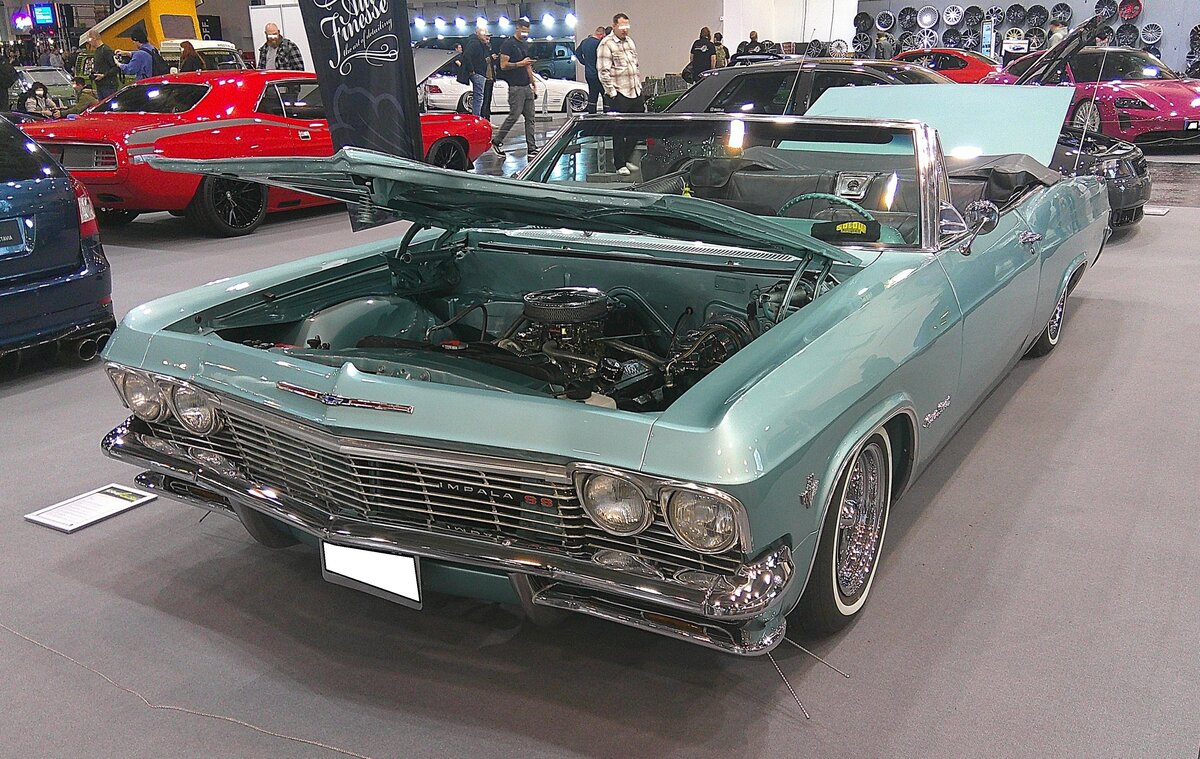 Chevrolet Impala SS Convertible Series 166 aus dem Jahr 1965 im Farbton artesian turquoise. Somit gehört dieses Cabriolet zur so genannten vierten Generation der Modellreihe  Impala . die eben ab 1965 bei den Chevrolet-Dealern stand. Im Modelljahr 1965 war der  Impala  das Spitzenmodell im Verkaufsprospekt von Chevrolet. Für die mittlere Baureihe stand der  Bel Air  und als Basismodell galt der Biscayne. Toppmotorisierung war ein V8-Motor mit einem Hubraum von 6489 cm³. Je nach Vergaserbestückung betrug das Leistungsspektrum zwischen 325 PS und 425 PS. Essen Motor Show am 28.11.2025.