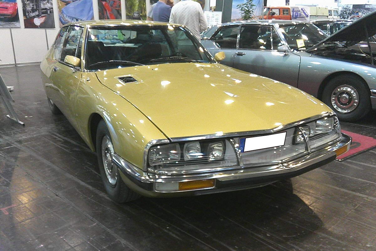Citroen SM im Farbton or de simiane. Von 1970 bis 1975 wurden 12.920 Fahrzeuge dieses Typs produziert. Die V6-Motoren stammten aus dem Regal von Maserati. Verantwortlich für die Motorenentwicklung zeichnete sich der geniale Giulio Alfieri (*1924 +2002). Bis 1974 hatte der Motor einen Hubraum von 2675 cm³ und leistete zwischen 170 PS und 178 PS. Im letzten Modelljahr hatte der V6-Motor einen Hubraum von 2965 cm³ und eine Leistung von 180 PS. Die Typbezeichnung SM soll angeblich  Serie Maserati  heißen. Retro Classics in Essen am 09.04.2026.