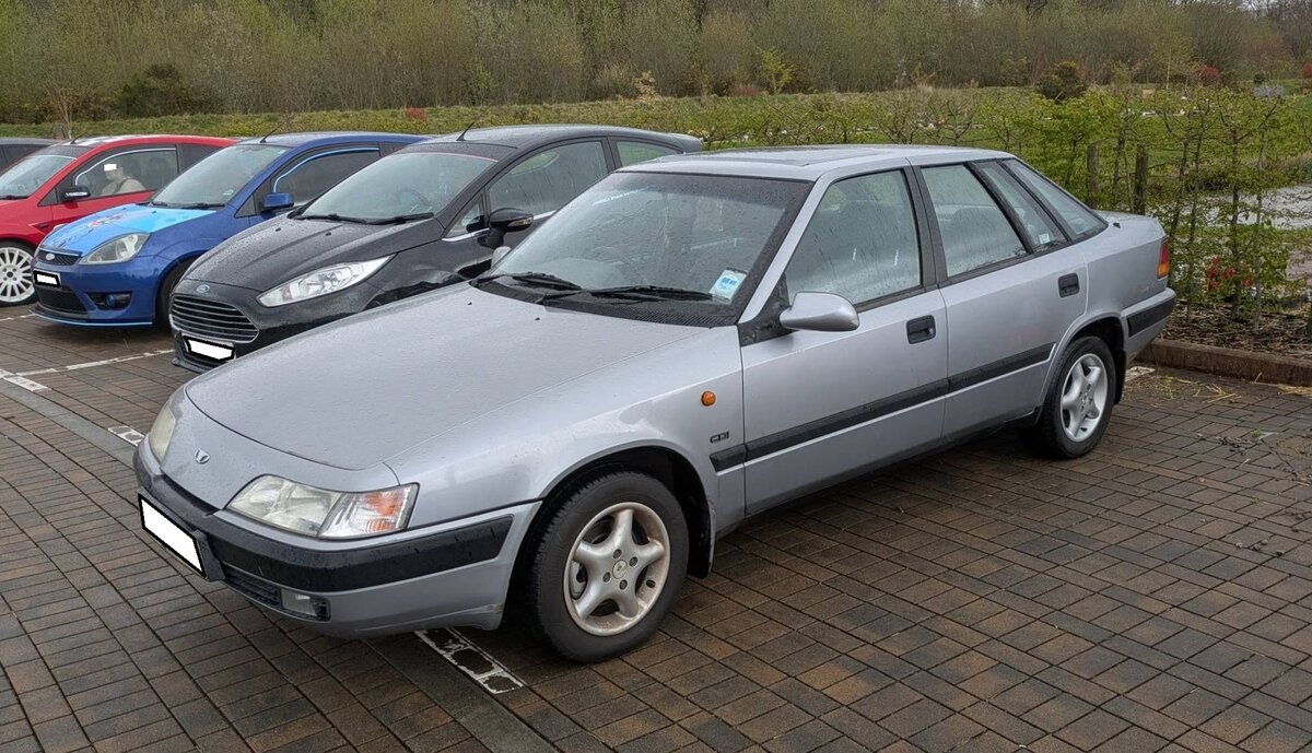 Daewoo Espero CDI aus dem Jahr 1996. Der Daewoo Espero war eine viert�rige Mittelklasselimousine, die beim italienischen Designstudio Bertone gezeichnet wurde. Produziert wurde das Modell in S�dkorea. Das Modell wurde ab 1990 produziert und gelangte ab Mitte 1995 auch bei uns in Europa zum Verkauf. Aufgebaut war das Modell auf der so genannten J-Plattform des Opel Ascona C. Der Espero war ausschlie�lich als Stufenhecklimousine mit Vorderradantrieb verf�gbar. Das Modell war, zumindestes bei uns in Deutschland, mit drei verschiedenen Vierzylinderreihenmotoren lieferbar. Die allermeisten Kunden w�hlten die Toppmotorisierung, einen Vierzylinderreihenmotor mit einem Hubraum von 1998 cm� und einer Leistung von 105 PS. Sirhowy Valley (S�dwales) Classic car meeting im April 2025.