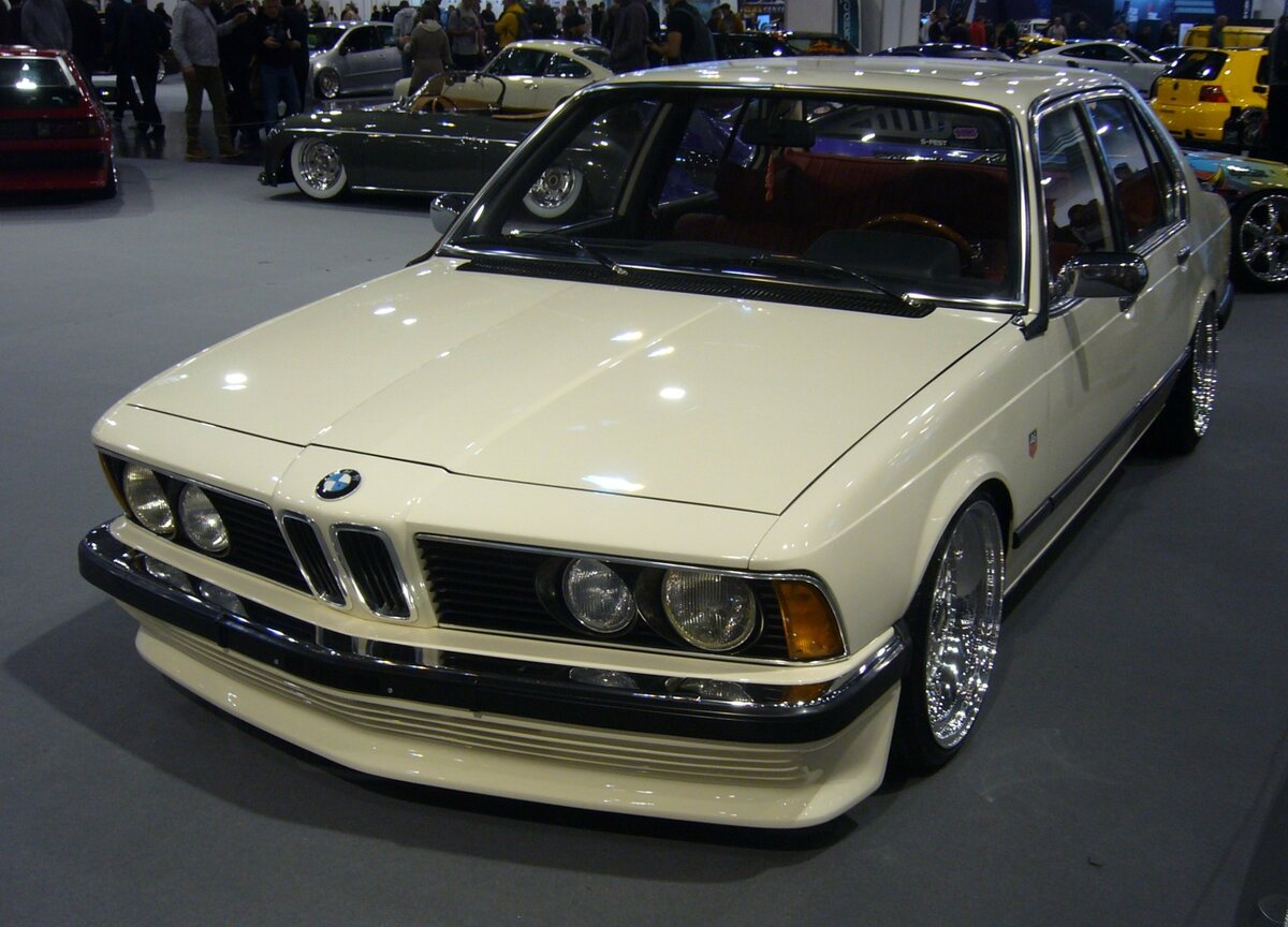 Ein etwas  aufgepimpter  BMW E23 728 im Farbton chamonixweiß aus dem Jahr 1978. Als Nachfolger des bisherigen BMW E3 erschien im Mai 1977 die Baureihe E23, besser bekannt als 7´er Reihe. Das Modell war anfänglich als BMW 728, BMW 730 und BMW 733i lieferbar. Bei seiner Markteinführung war ein solcher BMW 728 ab einem Kaufpreis von DM 29.300,00 zu haben. Serienmäßig hatte der BMW 728 einen Sechszylinderreihenmotor mit einem Hubraum von 2788 cm³ mit einer Leistung von 170 PS. Durch einige technische Verfeinerungen leistet der gezeigte E23 allerdings 241 PS bei unverändertem Hubraum. Essen Motorshow am 06.12.2023.