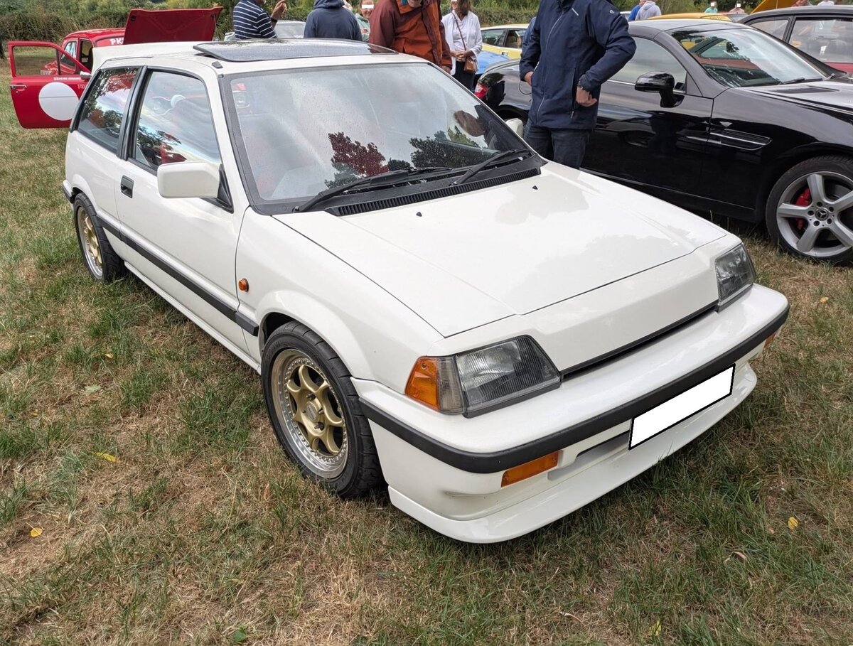 Ein etwas  aufgepimpter  Honda Civic MK3 aus dem Jahr 1986. Im Oktober 1973 brachte Honda in Deutschland den ersten Civic auf den Markt. Mit einem modernen Konzept trat der Wagen in Europa gegen solche Typen wie Fiat 127, Renault R5 und Peugeot 104 an und war dabei erfolgreich. Hier konnte ich einen Civic der dritten Generation, wie er von 1983 bis 1987 produziert wurde, ablichten. Das Modell war als zweit�rige Steilhecklimousine, als Kombimodell namens  Shuttle , sowie in der sportlichen Coupe-Version namens CRX lieferbar. Der Civic war mit etlichen Motorisierungen lieferbar. Das gezeigte Auto ist mit dem Vierzylinderreihenmotor mit einem Hubraum von 1488 cm� und serienm��igen 85 PS motorisiert. Treffen des Chainbridge classic car club auf der Wiese vor einem Pub in Chainbridge/Wales im Juli 2025.