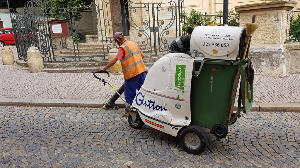 Ein motorisierter selbstfahrender Straßen Staubsauger, der mit einer Handgabel geführt wird. Der aufgenommene Schmutz wird direkt in eine Mülltonne geblasen, welche schnell gewechselt werden kann. Gesehen am 20.6.2018 in der Altstadt von Kutna Hora.