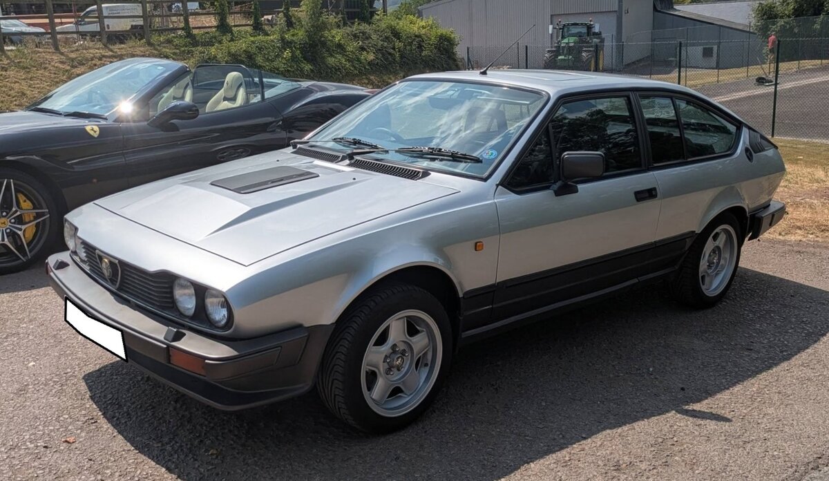 Ein rechts gelenkter Alfa Romeo GTV 6 2.5 Litri im Farbton argento. Das Oberklassemodell Alfetta erschien 1972 als viert�rige Limousine. Wie bei den  Milanesen  �blich, folgte einige Zeit sp�ter, in diesem Fall im Jahr 1974, eine Coupe-Version. Aufgrund seiner Korrosionsanf�lligkeit war dem GT bzw. GTV in Deutschland kein besonders gro�er Verkaufserfolg beschienen. Unter der Motorhaube verrichtet in diesem Modell ein V6-Motor seine Arbeit. Aus einem Hubraum von 2492 cm� leistet dieser Motor 160 PS. Die H�chstgeschwindigkeit wurde damals von Alfa Romeo mit 205 km/h angegeben. Besucherparkplatz des Oldtimer-H�ndlers  Ignition Sheed  in Abergavenny/S�d Wales am 17.05.2025.