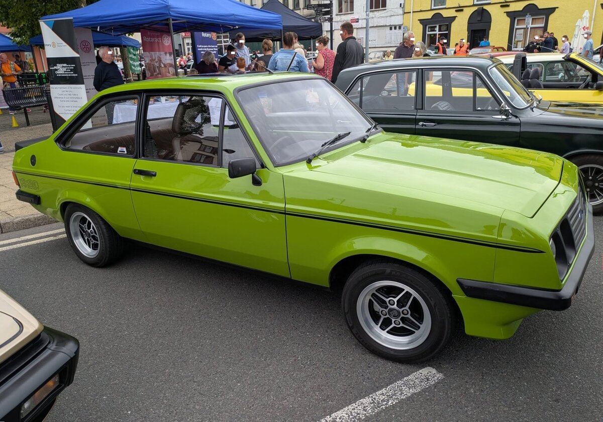 Ford Escort MK2 RS 2000 im Farbton java green. Der Escort MK2 wurde 1975 vorgestellt. Beworben als  Hochleistungs-Tourenwagen  stand der RS 2000 ab Ende 1975 bei den Ford Händlern und blieb bis zum Erscheinen des neuen Escort MK3, im September 1980 im Verkaufsrogramm. Serienmäßig leistet der Vierzylinderreihenmotor mit einem Hubraum von 1.993 cm³ 110 PS. Im Frühjahr 1976 stand eine solches Auto in Deutschland mit einem Grundpreis von DM 13.800,00 in den Preislisten. Classic car meeting in Brynmawr/South Wales am 27.07.2025.