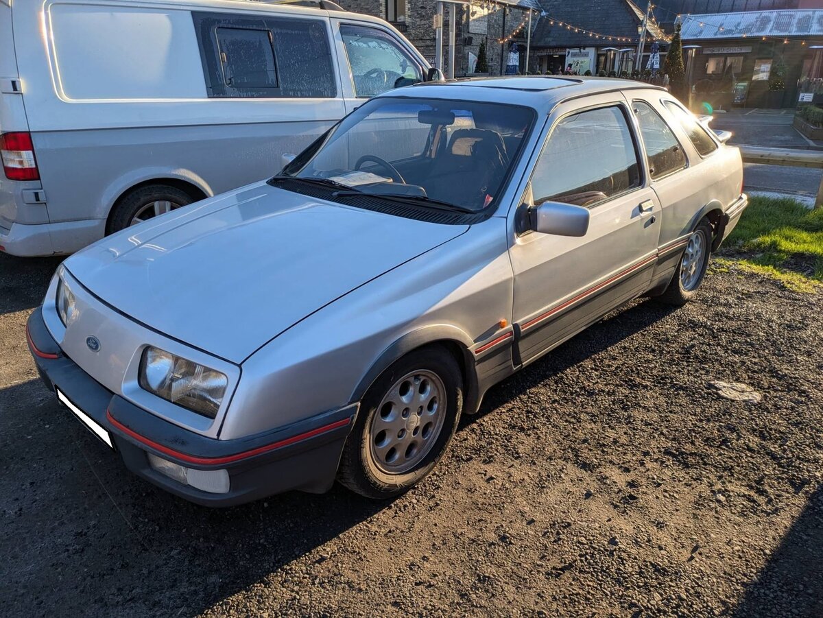 Ford Sierra XR4i der Modelljahre von 1983 bis 1985. Auf der Basis des ein Jahr vorher präsentierten Ford Sierra brachten die britischen und deutschen Ford-Werke im März 1983 das sportlich ausgelegte Modell Sierra XR4i auf den Markt. Optisch war das Modell an seinem doppelten Heckflügel und dem zweiten Seitenfenster hinter der C-Säule zu erkennen. Auch die so genannten  Käseloch-Felgen  waren ein  Eyecatcher . Europaweit wurden 25.662 Autos dieses Typs gebaut. Mit einem Basispreis in Deutschland von DM 29.000,00, war der XR4i nur unwesentlich günstiger als ein Porsche 924. Unter der Motorhaube verrichtet (bei den deutschen Modellen) ein V6-Motor mit einem Hubraum von 2772 cm³ und einer Leistung von 150 PS seinen Dienst. September 2024 auf dem Besucherparkplatz eines Pubs in Pont-Neddfechan/South Wales.