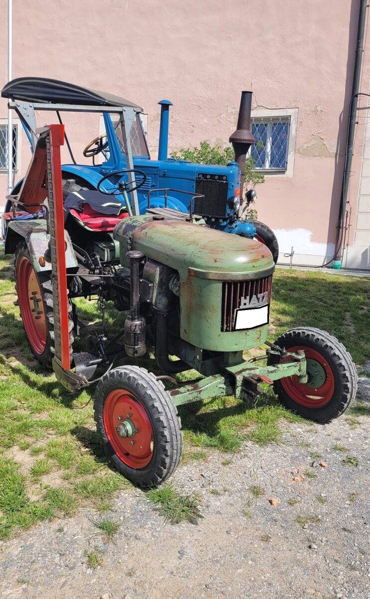 Hatz Traktor mit M�hbalken. Ich vermute mal das es sich um den Typ TL 18 handelt. Hatz mit Sitz im niederbayerischen Ruhstorf an der Rott ist ein gestandener Motoren-Hersteller, der auch heute noch gut im Gesch�ft ist. Von 1953 bis 1964 wurden aber auch insgesamt 7201 Traktoren der verschiedensten Baureihen produziert. Zu Beginn der sechziger Jahre kam es nicht nur bei Hatz zu einer Absatzkrise im Schleppergesch�ft. 1964 beschloss die Gesch�ftsf�hrung den Ausstieg aus der Schlepperproduktion und eine R�ckorientierung auf den florierenden Bau von Kleindieseln. Welches Mitglied aus dem Plenum kann denn bei der genauen Identifikation des Acherschleppers helfen? Oldtimertreffen Altenthann/Oberpfalz am 03.05.2026.
