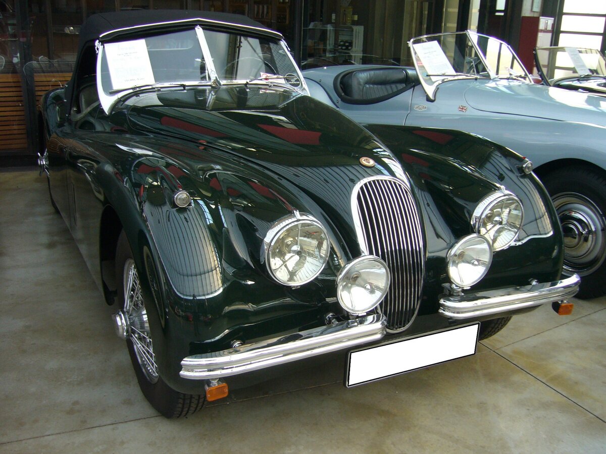 Jaguar XK 120 OTS aus dem Jahr 1953. Der Jaguar XK120 wurde in den Jahren von 1948 bis 1954 gebaut. Hier wurde ein XK120 OTS abgelichtet. Das OTS steht für O pen T wo S eater. Im Laufe der Produktionszeit kam noch das Modell FHC ( F ixed H ead C oupe) und DHC (D rop H ead C oupe) hinzu. Der im Farbton british racing green lackierte XK120 wurde im Juli 1953 erstmalig zugelassen. Er hat einen Sechszylinderreihenmotor, der aus einem Hubraum von 3442 cm³ in diesem Fahrzeug 160 PS leistet. Je nach gewählter Achsübersetzung, soll die Höchstgeschwindigkeit zwischen 180 km/h und 210 km/h gelegen haben. Classic Remise Düsseldorf am 20.07.2022.