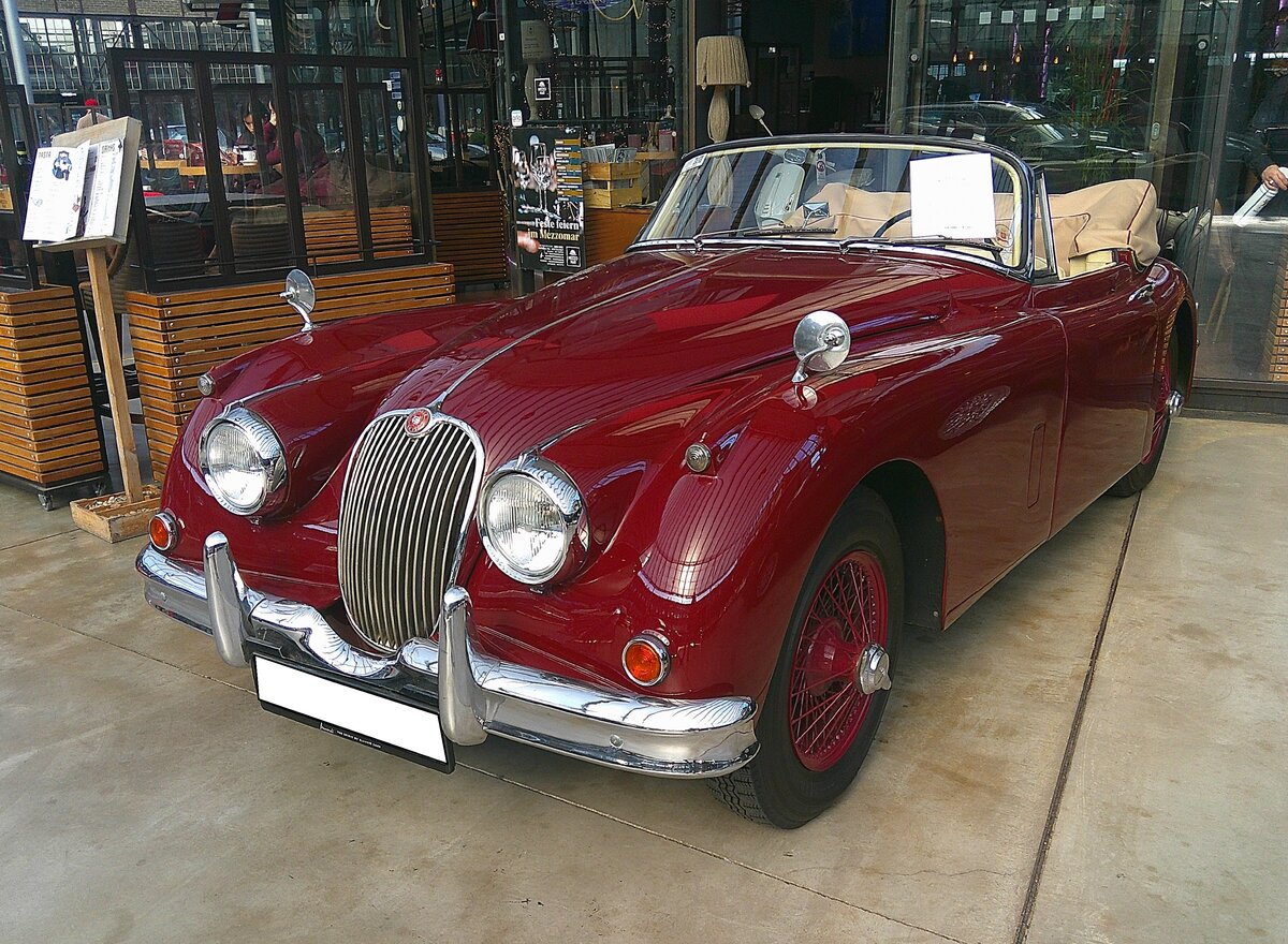 Jaguar XK150 DHC, gebaut in den Jahren von 1957 bis 1961. DHC steht für D rop H ead C oupe, also Cabriolet. Der XK150 war das letzte Modell der legendären XK-Baureihe. 1957 gewann ein XK150 das 24 Stunden Rennen von Le Mans. Der Sechszylinderreihenmotor hat einen Hubraum von 3442 cm³ und leistet zwischen 193 PS und 213 PS. Ab dem Modelljahr 1959 war auch ein aufgebohrter Motor mit 3781 cm³ Hubraum und 223 PS lieferbar. Der gezeigte Wagen verließ im Jahr 1958 die Werkshallen in Coventry und wurde ins kalifornische Los Angeles ausgeliefert. Classic Remise Düsseldorf am 02.03.2026.