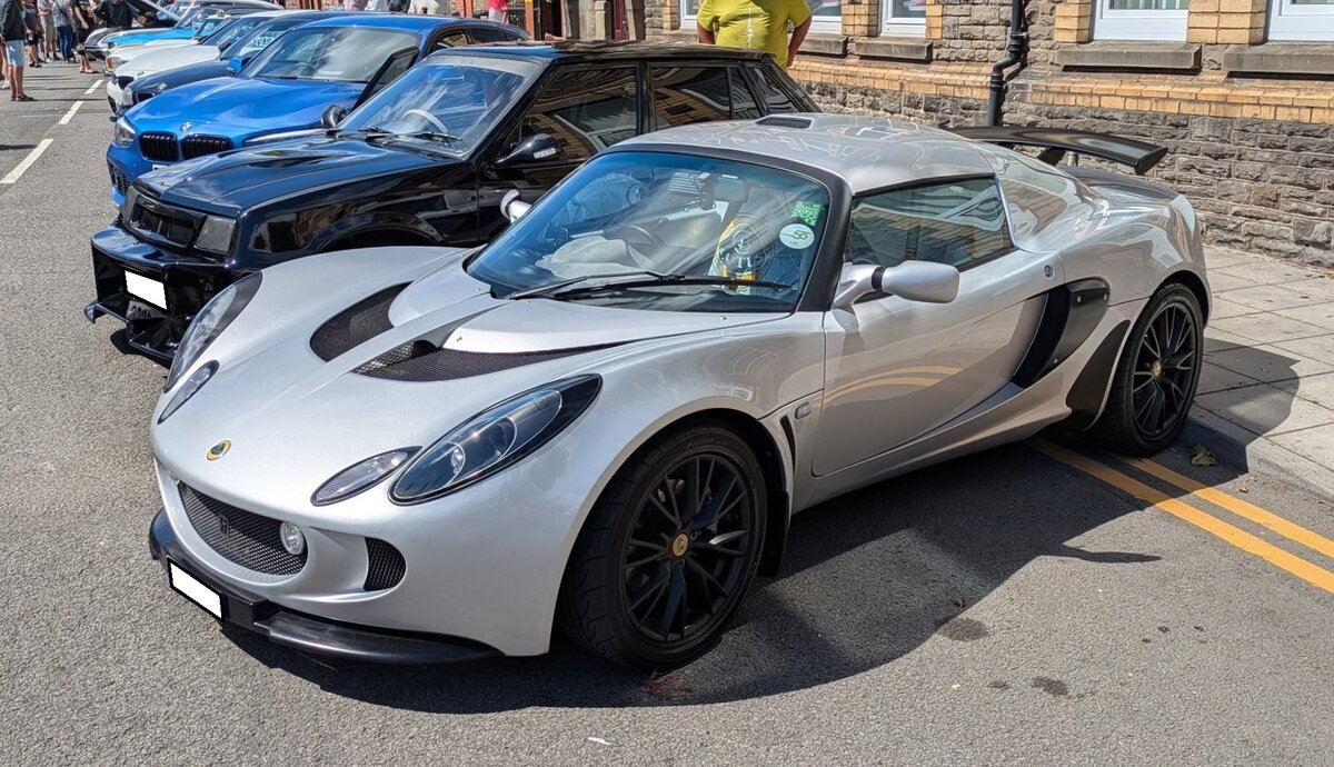 Lotus Exige S Coupe. Zwischen dem Jahr 2000 und 2021 wurde dieser handliche Sportwagen als Coupe und Targa-Modell in etlichen Motorisierungsversionen bei Lotus im englischen Hethel/Grafschaft Norfolk in Handarbeit montiert. Der hier gezeigte Exige aus dem Jahr 2006 geh�rt somit zur Series 2, die von 2004 bis 2011 gebaut wurde. In dieser Serie wurde ein Vierzylinderreihenmotor mit Kompressor-Aufladung aus dem Hause Toyota verbaut. Dieser hat einen Hubraum von 1796 cm� und leistet, je nach Modelljahr 192 PS, 240 PS oder 260 PS. Brynmawr Classic Car Show/South Wales am 26.07.2026.