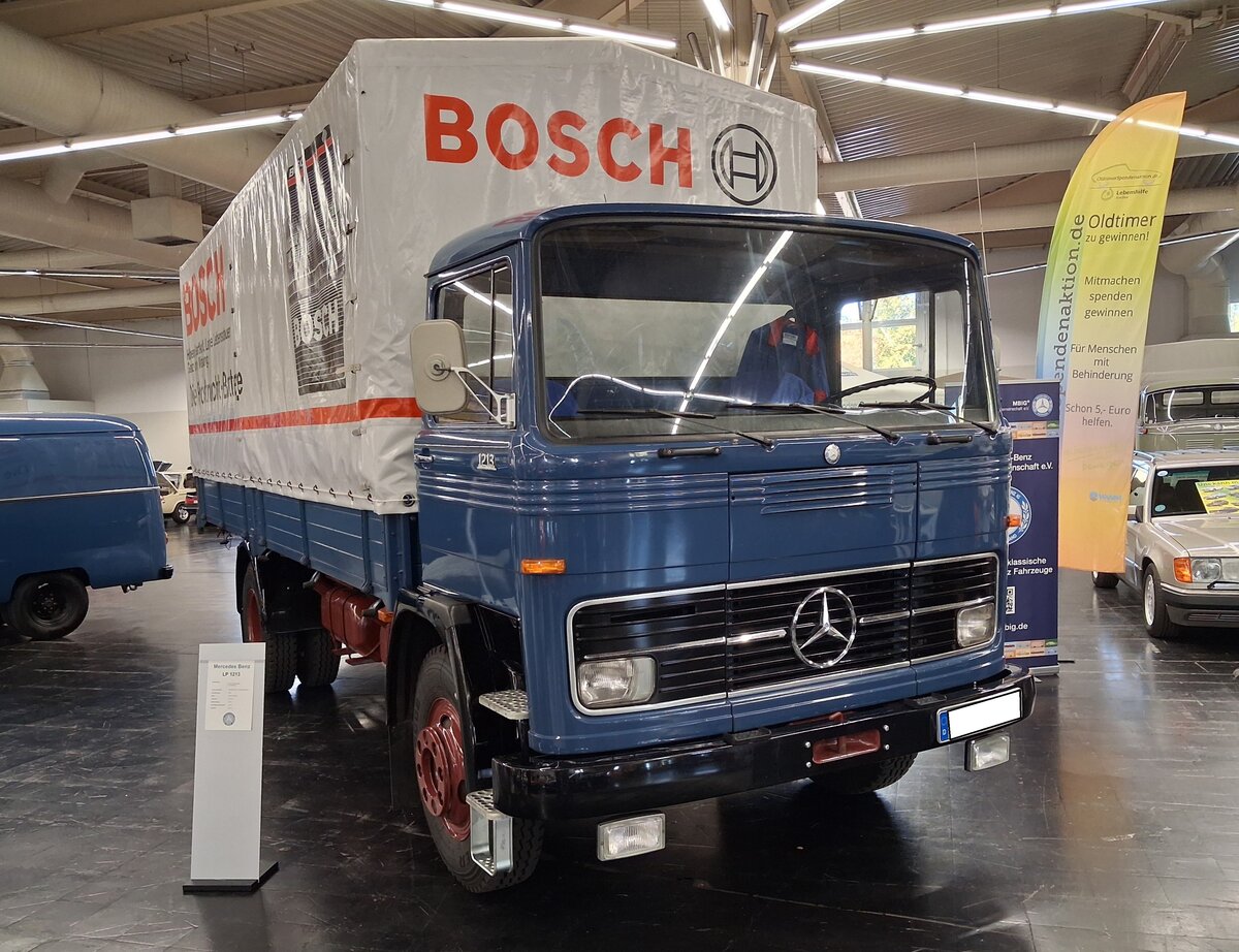 Mercedes Benz LP1213 aus dem Jahr 1966. Gebaut wurde der mittelschwere Frontlenker-LKW mit dem so genannten  kubischen  Fahrerhaus ab dem Jahr 1965. Die Baureihe pr�gte als neuentwickelter Frontlenker das Stra�enbild der sp�ten 1960´er und 1970`er Jahre in Deutschland stark mit und l�ste zum gr��ten Teil die klassischen Kurzhauber-LKW`s ab. Produziert wurden die Lastwagen im Mercedes Benz Werk in W�rth/Rheinland-Pfalz. Die Kabinen besa�en in dieser mittleren Gewichtsklasse Scheinwerfer im unteren Bereich des K�hlergrills, verf�gten jedoch damals noch nicht �ber eine kippbare Kabine. Dieser LP1213 ist in der Farbkombination LKW-blau 5328/ochsenblut 3575 lackiert und hat eine Nutzlast von 5900 Kilogramm. Der Erstbesitzer hat damals eine Servolenkung und zus�tzliche Nebelscheinwerfer mit bestellt. Als Antrieb dient dem Truck ein Sechszylinderdieselmotor vom Typ OM352. Dieser hat einen Hubraum von 5676 cm� und leistet 130 PS. Als maximale Geschwindigkeit gab man 91 km/h an. 
