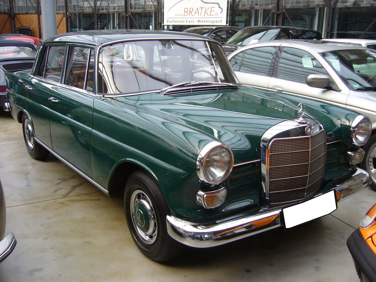 Mercedes Benz W110 230 Automatic, gebaut von 1965 bis 1968. Die  kleine Heckflosse  erschien bereits im Jahr 1961 und war mit einem 1.897 cm³ Vierzylinderreihenbenzinmotor = Modell 190 oder einem 1.988 cm³ Vierzylinderreihendieselmotor = Modell 200D lieferbar. 1965 erhielt die W110 Baureihe ein Facelift, mit dem das Modell bis 1968 weiter gebaut wurde. Ab diesem Zeitraum war der W110 auch als 230, mit einem Sechszylinderreihenmotor lieferbar. Dieser  Sechsender  hat einen Hubraum von 2281 cm³ und leistet bei seinem Erscheinen 105 PS. Im Modelljahr 1966, aus dem auch dieser Wagen stammt, erhöhte sich die Leistung auf 120 PS. Der Wagen ist im Farbton 268 dunkelgrün lackiert. Classic Remise Düsseldorf am 15.08.2021.