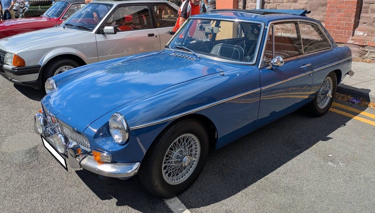 MG B GT 1800. Der MG B Roadster wurde bereits 1962 eingef�hrt. Im Oktober 1965 kam der als 2+2 Sitzer ausgelegte MG B GT zus�tzlich auf den Markt. Er war, genau wie der Roadster, bis 1980 im Verkaufsprogramm der Marke aus Coventry. W�hrend sich das Roadster Modell rund 400.000 mal verkaufte, wurde vom GT Modell genau 125.282 Einheiten abgesetzt. Der Vierzylinderreihenmotor hat einen Hubraum von 1798 und leistet 92 PS. Die H�chstgeschwindigkeit lag bei 168 km/h. Der gezeigte Wagen wurde im Jahr 1966 produziert und d�rfte im Farbton mineral blue lackiert sein. Brynmawr Classic Car Show/South Wales am 26.07.2026.