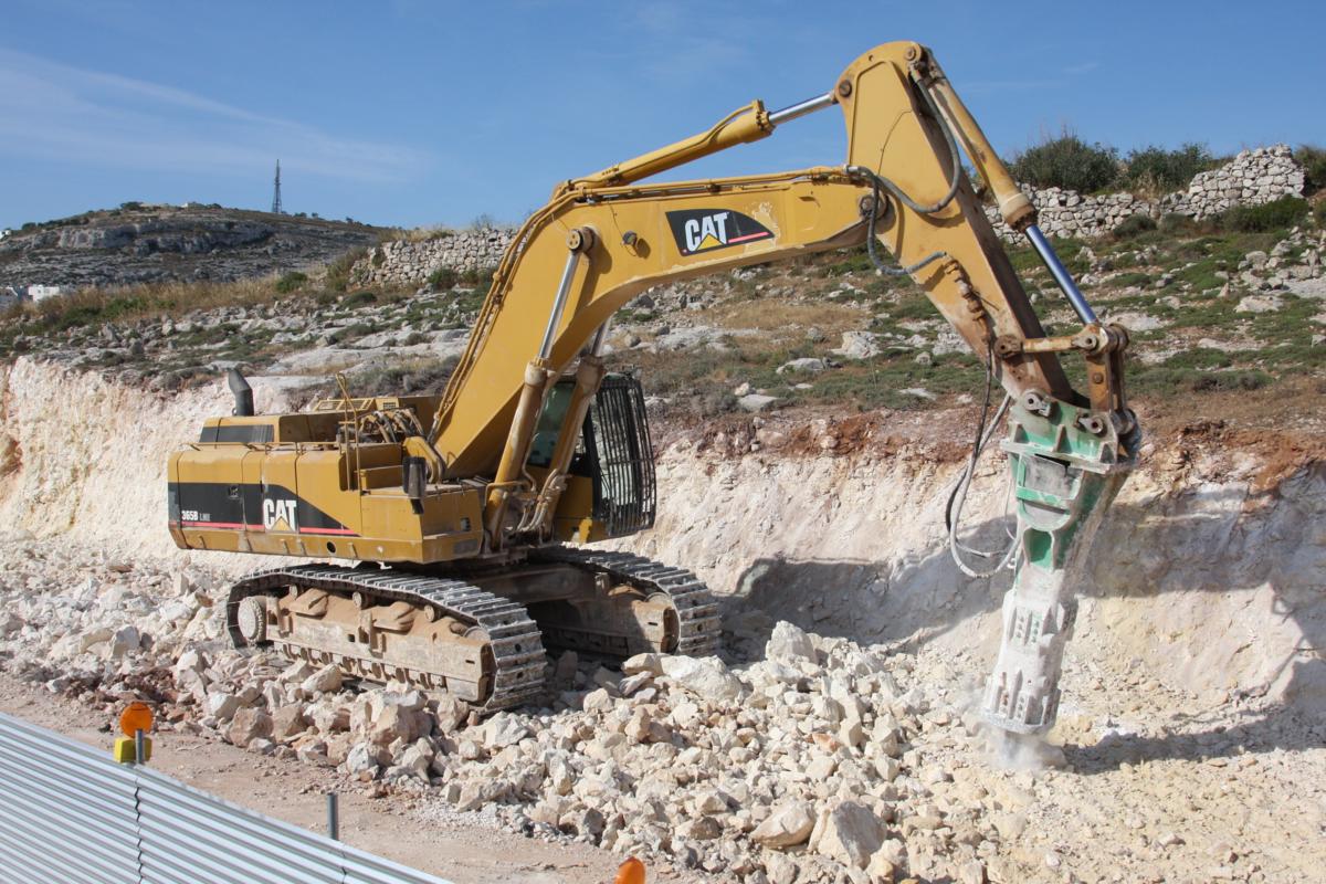 Mit mächtigem Bohrhammer als Vorsatzgerät ist dieser Caterpillar 365B LME am 12.5.2014 auf Malta bei Bugibba im Einsatz und bricht den Felsen auf. Zwischen Bugibba und St. George`s Bay wird derzeit die Küstenstraße neu gebaut.
