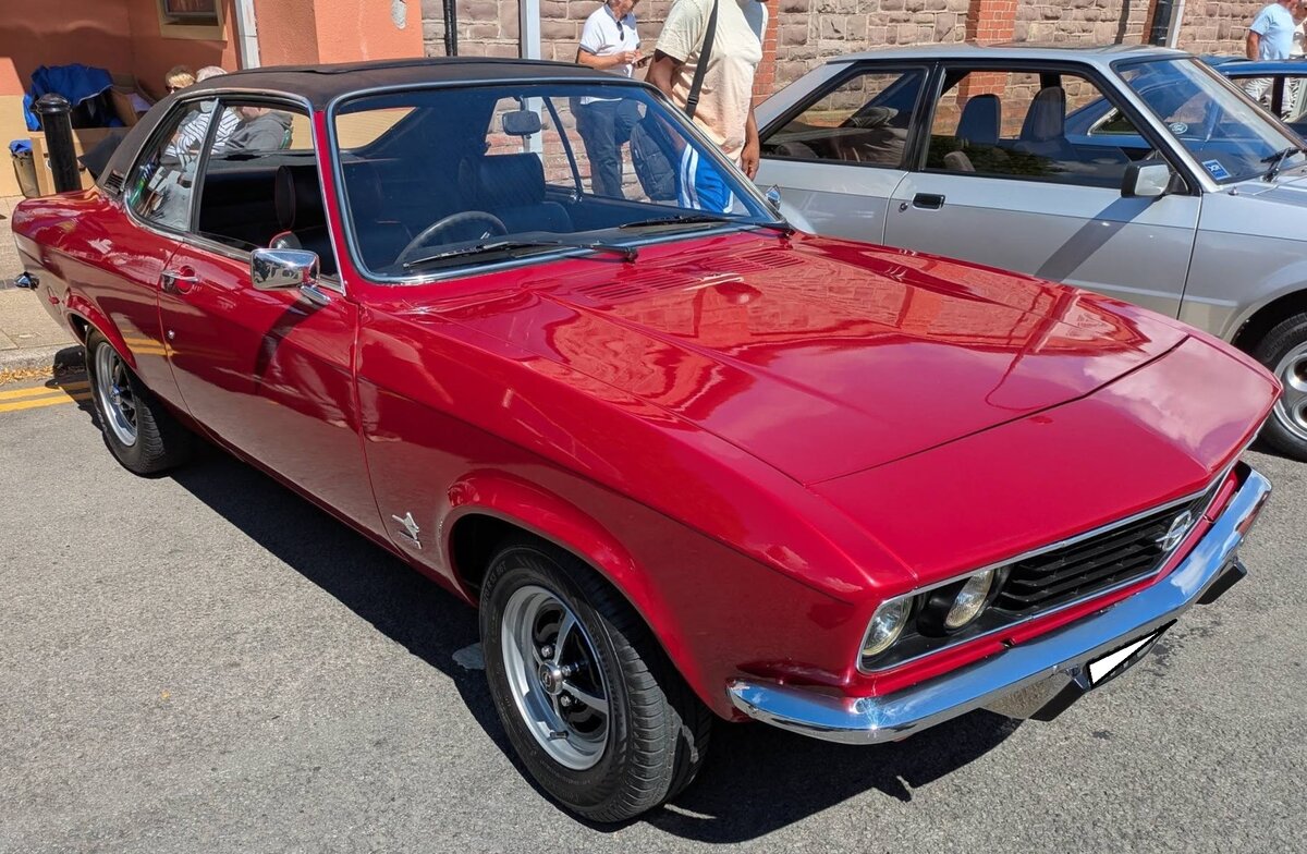 Opel Manta A, gebaut in den Jahren von 1970 bis 1975. Der Manta wurde als Konkurrenzprodukt zum sehr erfolgreichen Ford Capri, der ein Jahr vorher erschien, auf den Markt gebracht. Der Kunde konnte zwischen drei verschiedenen Vierzylinderreihenmotoren w�hlen: 1196 cm�, 1584 cm� und dem 1897 cm� Motor aus dem Opel Rekord. Die Leistung lag serienm��ig zwischen 60 PS und 105 PS. Der gezeigte, rechts gelenkte, Manta d�rfte im Farbton royalrot lackiert sein. Dieser Manta mit dem, zur Lackierung toll passenden Vinyldach, wurde im Februar 1972 erstmalig zum britischen Stra�enverkehr zugelassen. Was ich bei deutschen Manta A Modellen noch nie gesehen habe, ist ein solches Faltschiebedach? Brynmawr Classic Car Show/South Wales am 26.07.2026.