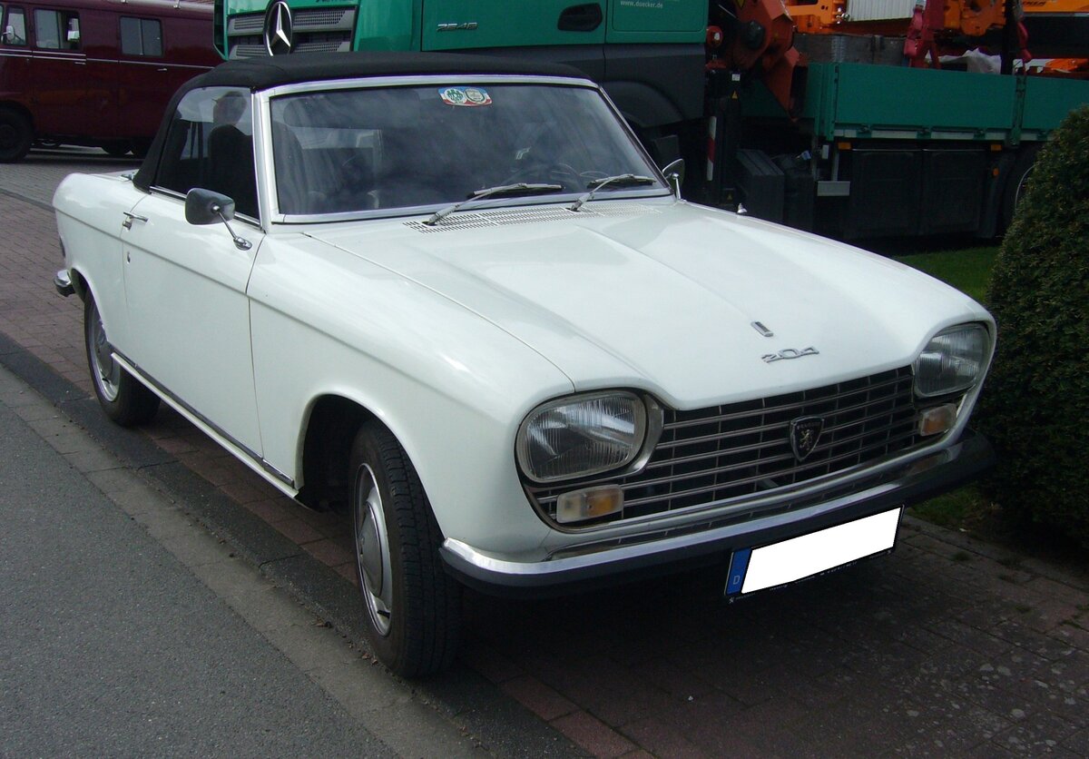 Peugeot 204 Cabriolet im Farbton blanc alaska. Der von Pininfarina gezeichnete Peugeot 204 kam im Frühsommer des Jahres 1965 auf den Markt. Anfang 1967 wurde die Modellpalette um folgende weitere Karosserieversionen erweitert: Es handelte sich um das gezeigte Cabriolet, ein dreitüriges Coupe und ein fünftüriges Kombimodell mit der Typbezeichnung Break. Der quer verbaute Vierzylinderreihenmotor hat einen Hubraum von 1130 cm³ und leistet, je nach Vergaserbestückung, 53 PS oder 58 PS. Oldtimertreffen beim Autohaus Voss in Rosendahl-Darfeld am 07.04.2024.