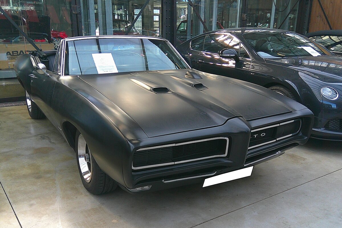 Pontiac GTO Convertible aus dem Jahr 1968. Von diesem Muscle-car setzte Pontiac im Modelljahr 1968 genau 9980 Fahrzeuge zu einem Preis ab US$ 3227,00 ab. Das Modell war auch in einer Coupeversion zu bekommen, die sich um ein vielfaches verkaufte. Motorisiert ist dieser black GTO mit einem V8-Motor mit einem Hubraum von 400 cui (6558 cm³). Der Erstbesitzer dieses Autos wählte damals das Modell mit einer Leistung von 265 PS. Durch eine andere Vergaserbestückung war sogar eine Leistung von 350 möglich. Classic Remise Düsseldorf am 02.03.2026.