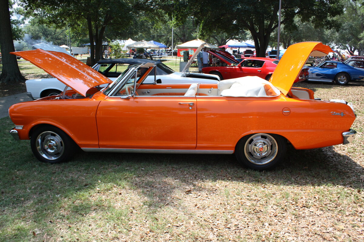 Profilansicht eines Chevrolet Nova II Convertible im Farbton omaha orange aus dem Jahr 1963. Das Midsize-Modell Nova II von Chevrolet kam 1962 auf den Markt. Es war als viertürige Limousine, zwei- oder viertüriger Station Wagon, als Coupe und Cabriolet lieferbar. Im Modelljahr 1963 konnte der Kunde den Wagen in den drei Series 100, 300 und 400, sowie in fünf verschiedene Ausstattungslinien bestellen. Bei der Motorisierung bestand die Wahlmöglichkeit zwischen einem 2.5l Vierzylinderreihenmotor mit 91 PS oder einem Sechszylinderreihenmotor mit einem Hubraum von 3186 cm³ und einer Leistung von 122 PS. Oldtimertreffen der Magnolia Classic Cruiser in Pascagoula/Jackson County/Mississippi im September 2021.