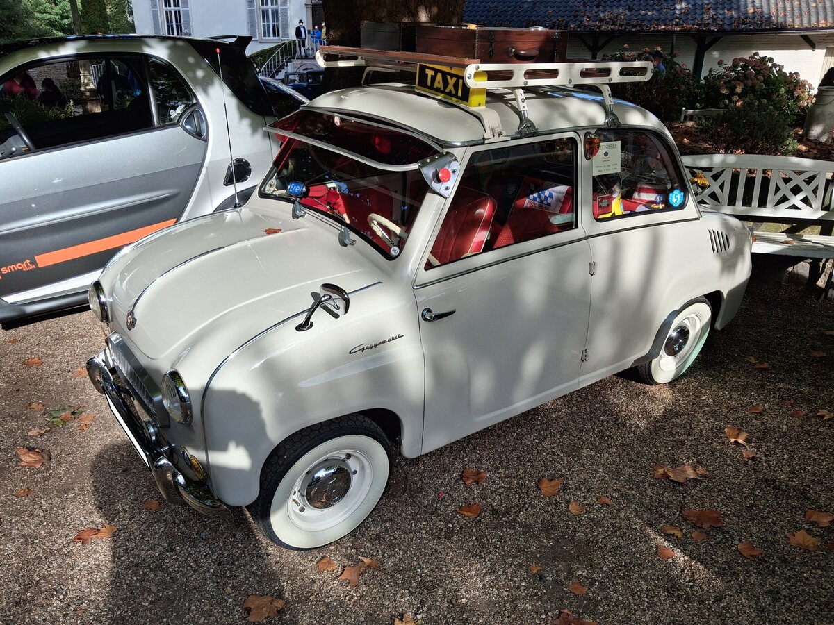 Profilansicht eines Glas Goggomobil T250 Limousine, gebaut von 1955 bis 1969 in Dingolfing. Vorgestellt wurde die winzige Limousine im Herbst 1954. Im Februar 1955 begann bei der Hans Glas GmbH die Serienfertigung. Der Wagen war auch als T300 und ab 1957 sogar als T400 lieferbar. Mehr als 75% der Fahrzeuge wurden allerdings mit dem 250 cm� Motor ausgeliefert. Diese Tatsache war den vielen Inhabern des  alten  F�hrerscheines der Klasse IV geschuldet. Hier handelt es sich um eine Limousine im Farbton astralwei�, die vor 1964 produziert wurde. Dieses ist an den, noch hinten, angeschlagenen T�ren zu erkennen. Der im Heck verbaute, Gebl�se-gek�hlte, Zweizylinderzweitaktmotor hat beim 250´er-Modell einen Hubraum von 247 cm� und leistet 13,6 PS. Ganz witzige Details an diesem  Goggo  sind der Dach- und der Heckgep�cktr�ger plus das Taxischild auf dem Dach. Cars & Castle auf Schlo� Lauersfort in Moers am 03.10.2026.