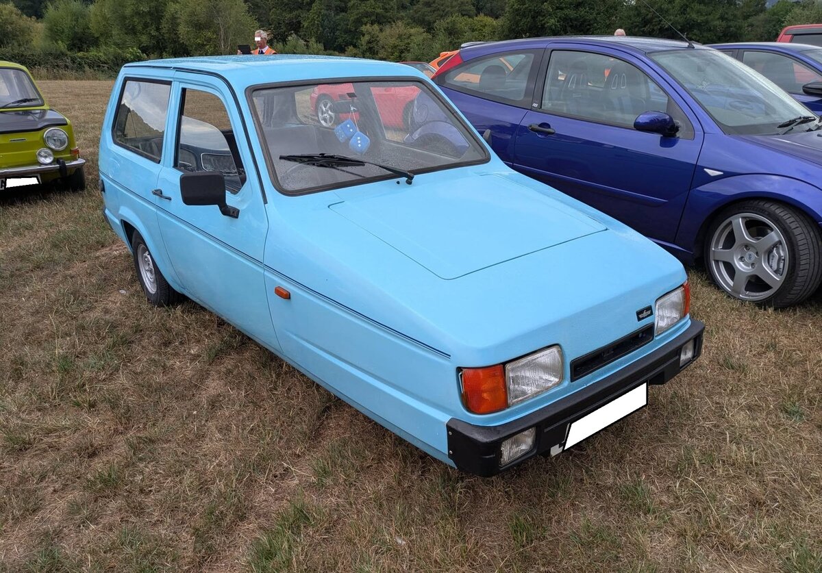 Reliant Robin MK2 in der  luxuri�sen  LX-Ausstattung. Wer kennt es nicht, das kultige, dreir�drige, Gef�hrt aus England. In Gro�britannien machten das geringe Gewicht von unter 450 kg und die drei R�der den  Robin  steuerlich zu einem Motorrad. Er durfte dort jahrelang mit einem einfachen Motorradf�hrerschein gefahren werden, was ihn besonders bei �lteren Fahrern beliebt machte. Das Modell wurde von 1973, mit einer Unterbrechung von einigen Jahren, bis ins Jahr 2001 von der Reliant Motor Company in Tamworth/Grafschaft Staffordshire gebaut. Die LX-Version war eine besser ausgestattete und h�herwertige Variante des Standard-Dreirads. Der Vierzylinderreihenmotor hat einen Hubraum von 848 cm� und leistet 41 PS. Die H�chstgeschwindigkeit soll bei  sporlichen  135 km/h liegen. Treffen des Chainbridge classic car club auf der Wiese vor einem Pub in Chainbridge/Wales im Juli 2025.