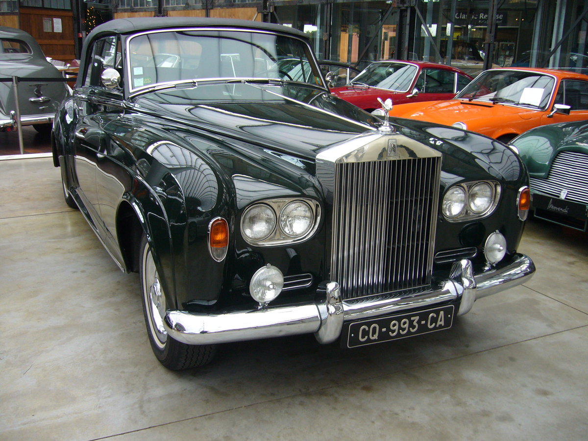 Rolls Royce Silver Cloud III Convertible, gebaut von 1962 bis 1965. Als der Silver Cloud III im Jahr 1962 vorgestellt wurde, fiel dem Fachpublikum als erstes der Wechsel zu Doppelscheinwerfern und eine niedriger geführte Linie der vorderen Kotflügel und der Motorhaube auf. Zum ersten Mal konnte auch für das Chassis des Rolls-Royce für den Aufbau einer Coupé- oder Cabriolet-Varianten bestellt werden, die bis dato exklusiv dem fast baugleichen Bentley Continental vorbehalten war. Der V8-Motor hat einen Hubraum von 6230 cm³ und leistet 187 PS. Classic Remise Düsseldorf am 26.11.2020.