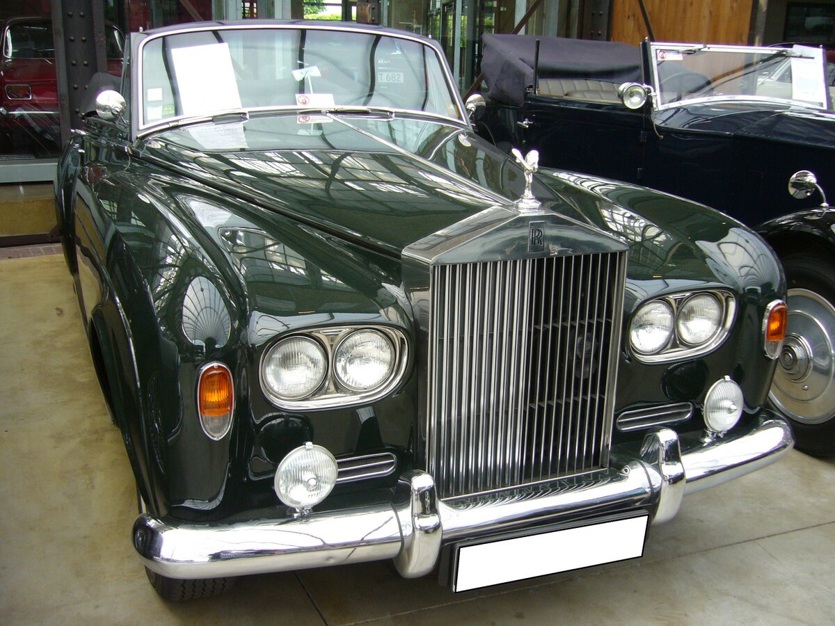 Rolls Royce Silver Cloud III Convertible aus dem Jahr 1964. Produziert wurde dieses Modell t von 1962 bis 1965. Als der Silver Cloud III im Jahr 1962 vorgestellt wurde, fiel dem Fachpublikum als erstes der Wechsel zu Doppelscheinwerfern und eine niedriger geführte Linie der vorderen Kotflügel und der Motorhaube auf. Zum ersten Mal konnte auch das Chassis des Rolls-Royce für den Aufbau einer Coupé- oder Cabriolet-Varianten bestellt werden, die bis dato exklusiv dem fast baugleichen Bentley Continental vorbehalten war. Der V8-Motor hat einen Hubraum von 6230 cm³ und leistet 187 PS. Dieser, im Farbton velvet green lackierte Silver Cloud III wurde 1964 gebaut und ist einer von nur 25 produzierten, linksgelenkten Silver Cloud III Convertible. Ein Vorbesitzer dieses Fahrzeuges ist der US-amerikanische Schauspieler Nicolas Cage. Classic Remise Düsseldorf am 30.12.2022.