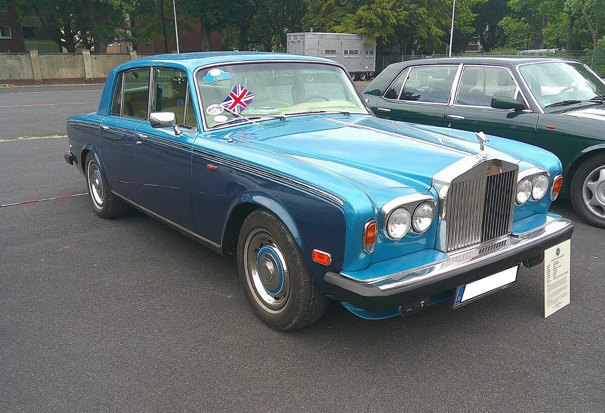 Rolls Royce Silver Shadow II, produziert von 1977 bis 1980. Als Silver Shadow wurde dieses Modell bereits im Jahr 1965 vorgestellt. Mit fast 29.000 verkauften Fahrzeugen in beiden Baureihen, war diese Baureihe  Silver Shadow  bis in die 1980´er Jahre das meist verkaufte Modell der Edelmarke aus dem englischen Crewe (Grafschaft Cheshire). Der V8-Motor, dieser Limousine hat einen Hubraum von 6750 cm� und leistet 201 PS. Der gezeigte Wagen, in der Farbkombination caribbean blue/coronation blue, wurde 1980 erstmalig in Palm Desert/Kalifornien zugelassen. Dieses ist auch an den vorderen und hinteren, seitlichen, Begrenzungsleuchten zu erkennen. 10. BCMM ( B ritish C ar M otorcycle M eeting) am 19.07.2026 an Mo´s Bikertreff in Krefeld.