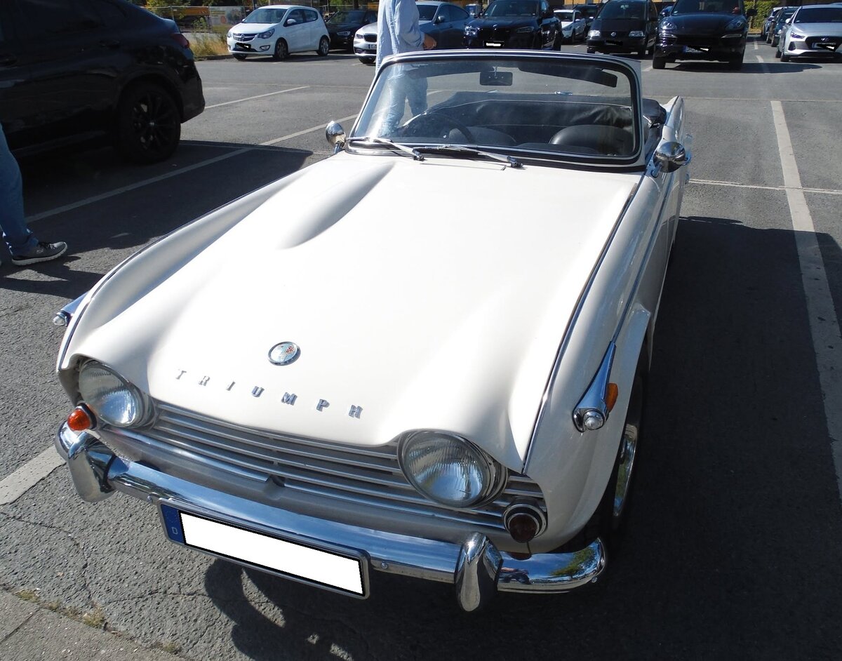 Triumph TR4A IRS, gebaut von 1965 bis 1967. Der TR4 wurde bereits 1961 vorgestellt. Im Jahr 1965 gab es einige Detailver�nderungen, die Gesetzes�nderungen in den USA geschuldet waren. Der Zusatz  IRS  weist darauf hin, das der Wagen mit einer unabh�ngigen, hinteren, Radaufh�ngung ausger�stet ist. Serie war eine hintere Starrachse. Der Vierzylinderreihenmotor leistet 104 PS aus einem Hubraum von 2138 cm�. Der gezeigte Wagen d�rfte im Farbton old english white lackiert sein. Oldtimertreffen am  Cafe del Sol  in Gelsenkirchen am 09.08.2026.