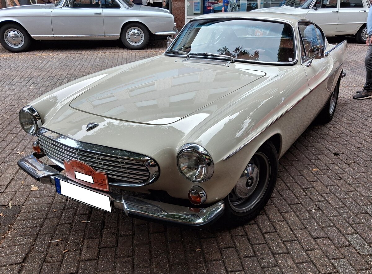 Volvo P 1800 S im Farbton vit (wei�), gebaut von 1963 bis 1972. Das von  Frua  gezeichnete Coupe stand bereits ab 1961 bei den Volvo-H�ndlern. Anfangs wurde der Wagen bei Jensen in West Bromwich/GB montiert. Aufgrund von Qualit�tsm�ngeln, wurde die Produktion im Jahr 1963 ins Volvo-Stammwerk Lundby bei G�teborg verlegt. Die hier produzierten Fahrzeuge sind am Buchstaben S (f�r Schweden bzw Sverige) in der Typenbezeichnung erkennbar. Von 1961 bis 1968 hatte der P1800 einen Vierzylinderreihenmotor mit einem Hubraum von 1778 cm� und einer Leistung zwischen 98 PS und 103 PS. Nach den Werksferien des Jahres 1968 wurde der sogenannte B20-Motor mit einem Hubraum von 1985 cm� und einer Leistung von 124 PS verbaut. 13. Saarner Oldtimer-Cup am 30.08.2026 in M�lheim an der Ruhr/Saarn.