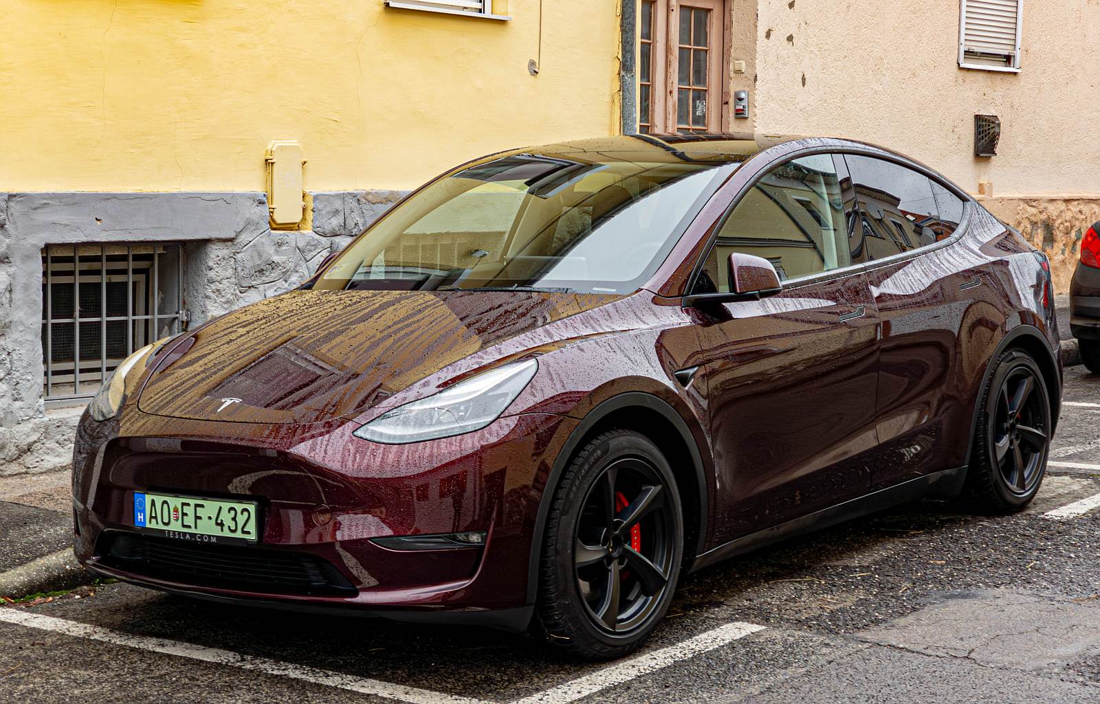 Hier ist ein Telsa Model Y in der Farbe Midnight Cherry beim regnerischen Wetter zu sehen.