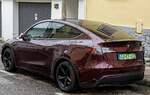 Hier ist ein Telsa Model Y von hinten, in der Farbe  Midnight Cherry  beim regnerischen Wetter zu sehen.