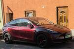 Hier ist ein Telsa Model Y in der Farbe Midnight Cherry beim sonnigen Wetter zu sehen.